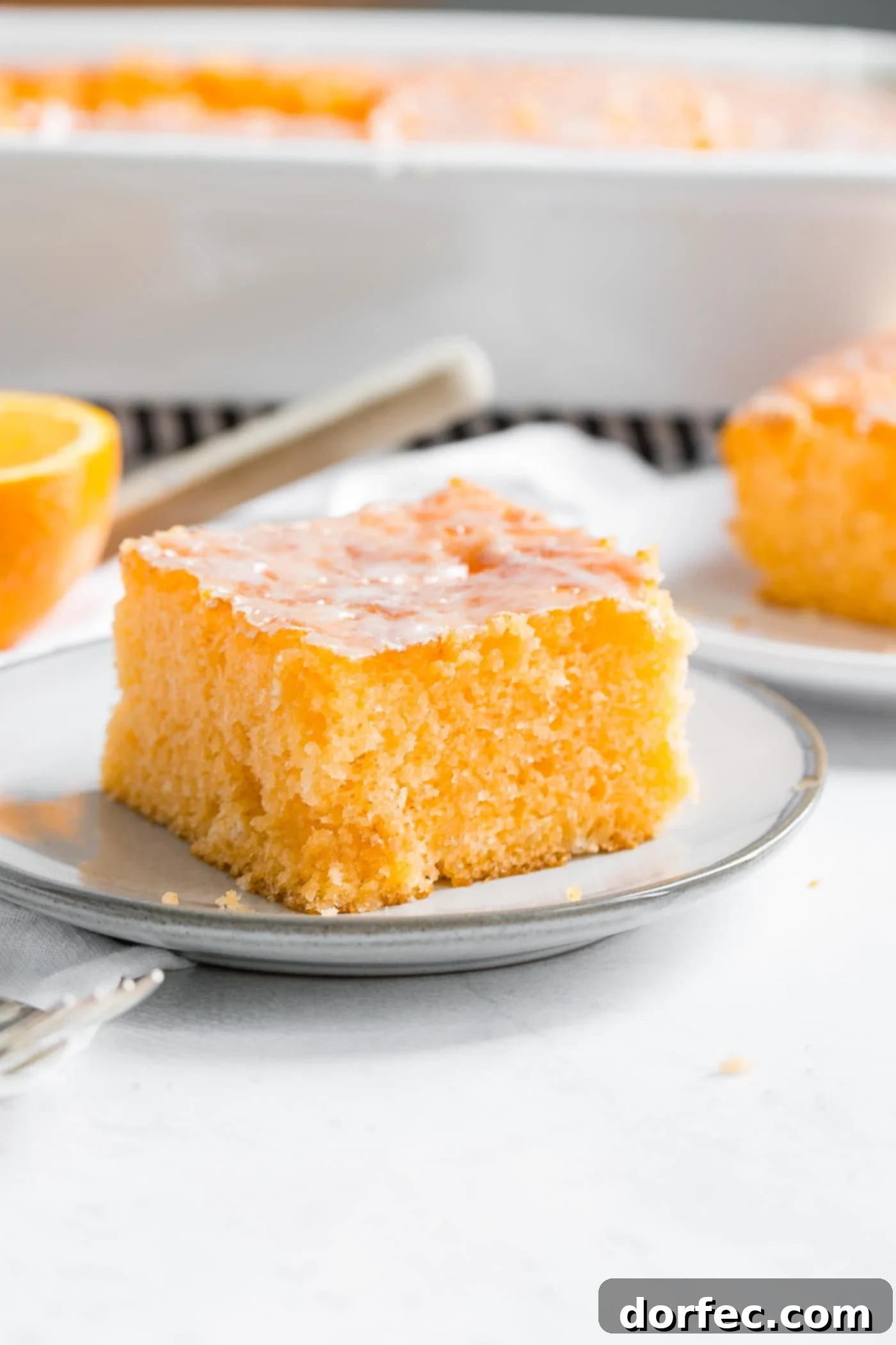 A photo of a piece of orange jello cake on a small white plate, showcasing the vibrant color and moist crumb.