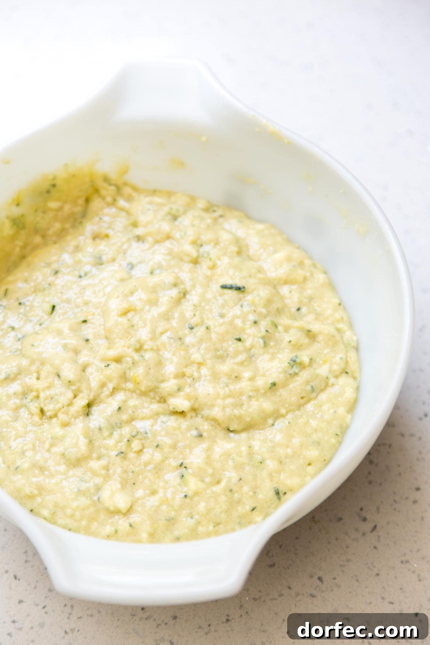 Lemon zucchini bread batter in a mixing bowl with shredded zucchini and lemon zest visible