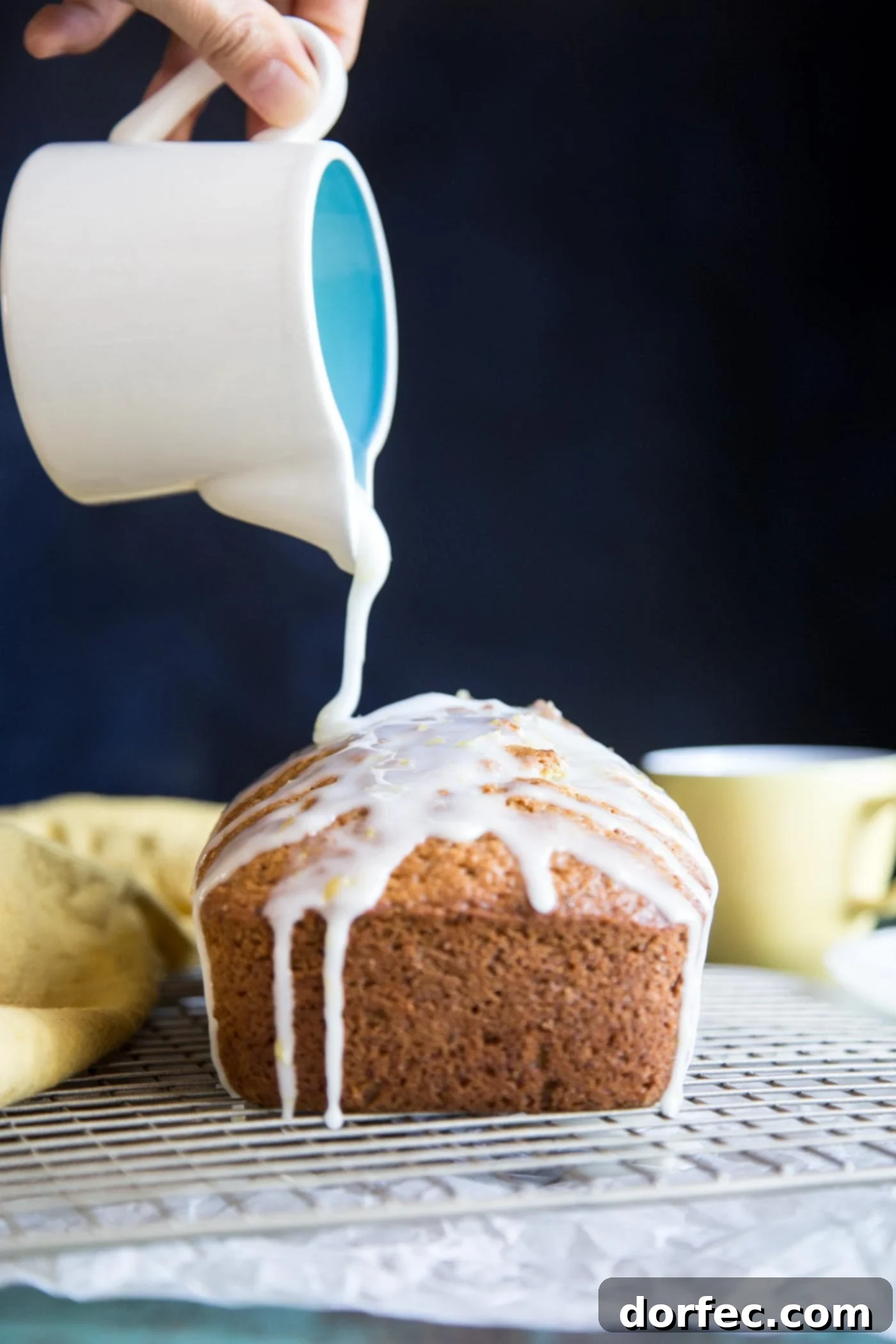 Pouring lemon glaze over a freshly baked lemon zucchini bread on a wire rack
