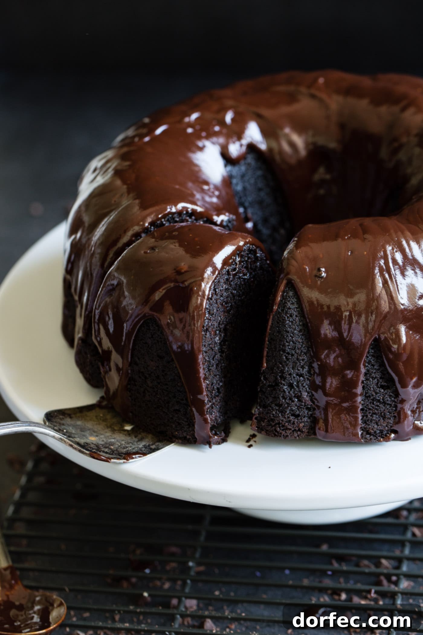 A slice of veggie cocoa cake being removed from the whole bundt cake. The cake has a dark glaze on it.