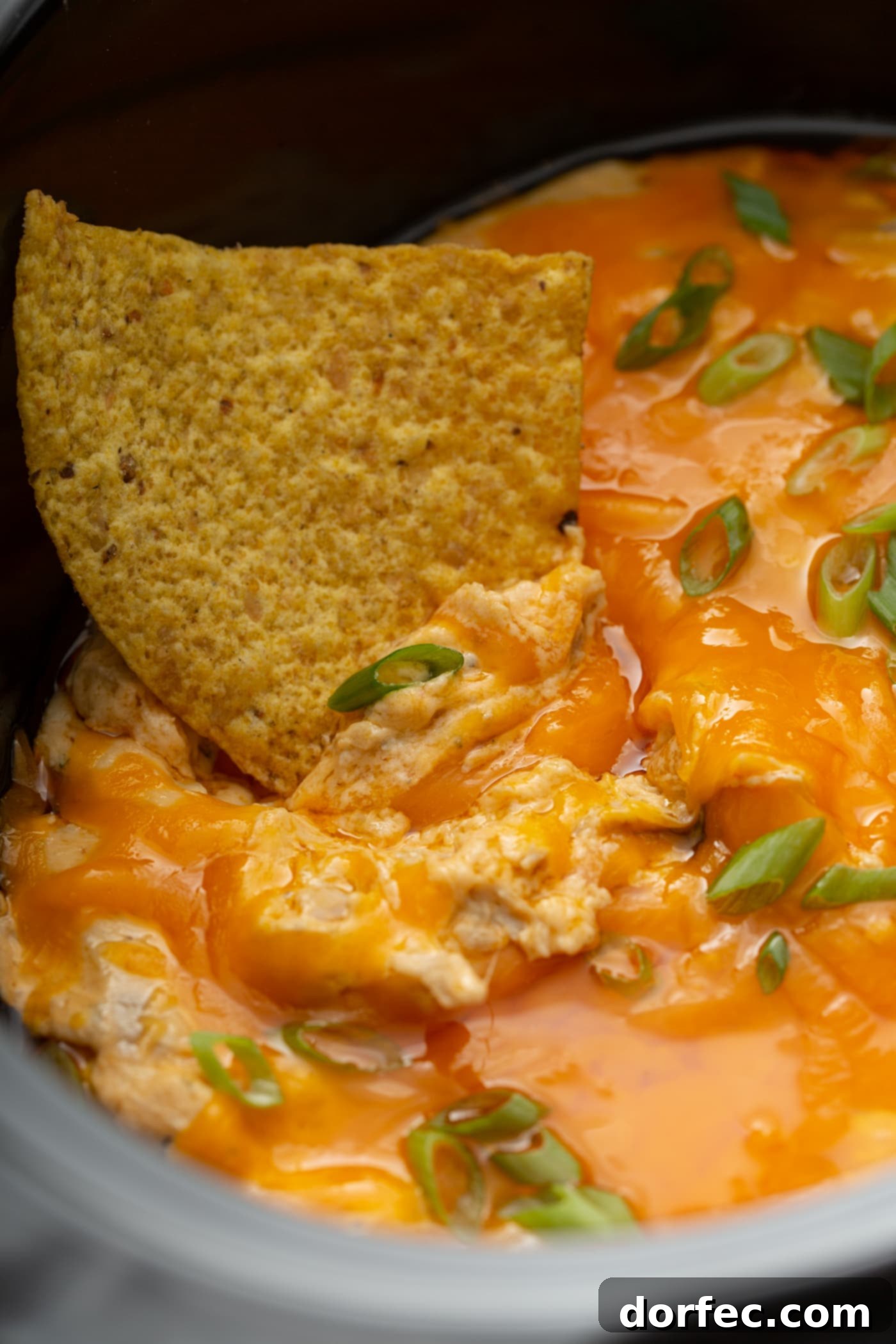 Creamy Slow Cooker Buffalo Chicken Dip on a Tortilla Chip A single tortilla chip generously loaded with creamy slow cooker buffalo chicken dip, revealing tender shredded chicken, rich buffalo sauce, and flecks of vibrant chopped green onions.