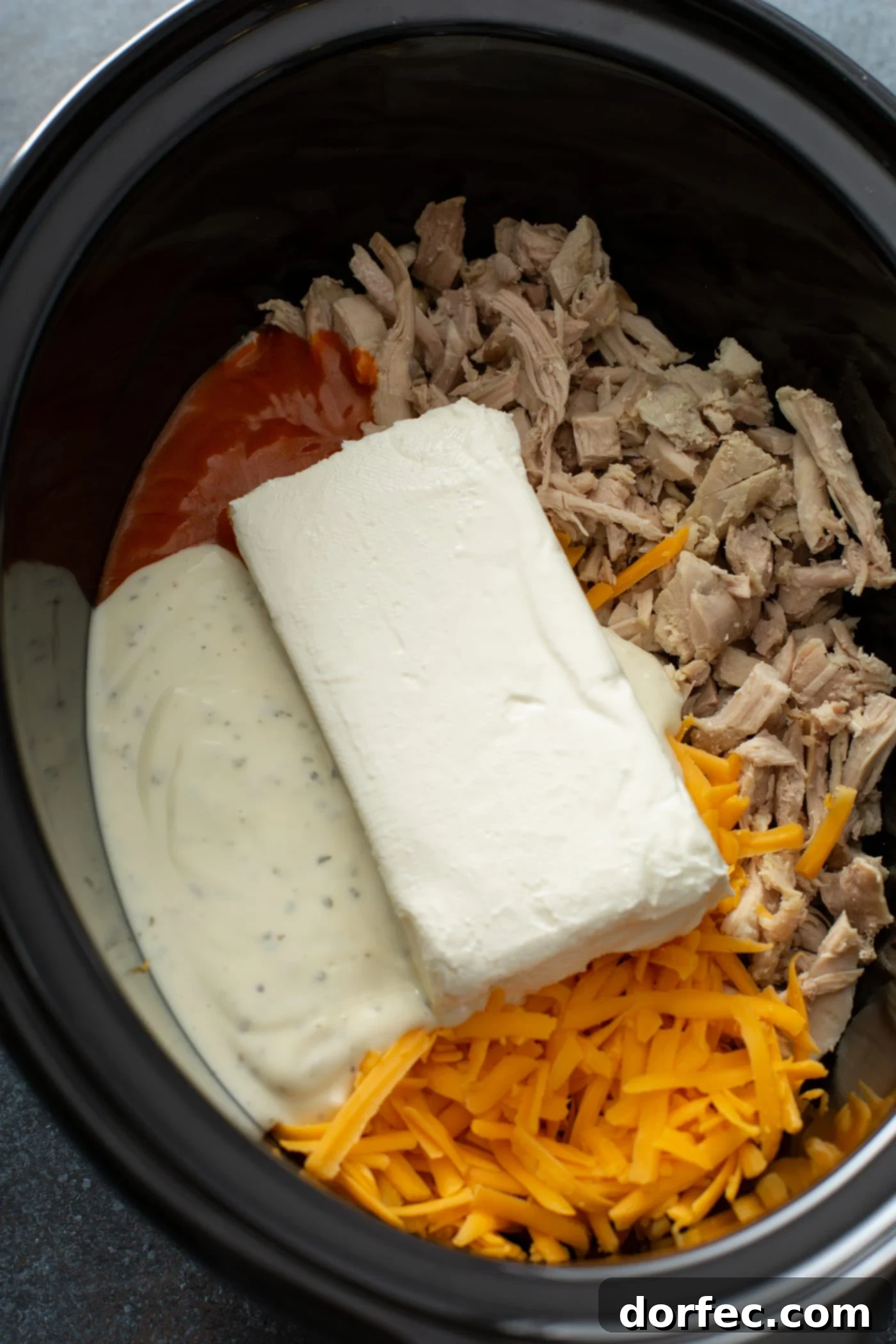Mixed Ingredients in the Slow Cooker A slow cooker filled with all the combined ingredients for buffalo chicken dip, showcasing shredded chicken, softened cream cheese, ranch dressing, and buffalo sauce, ready for cooking.