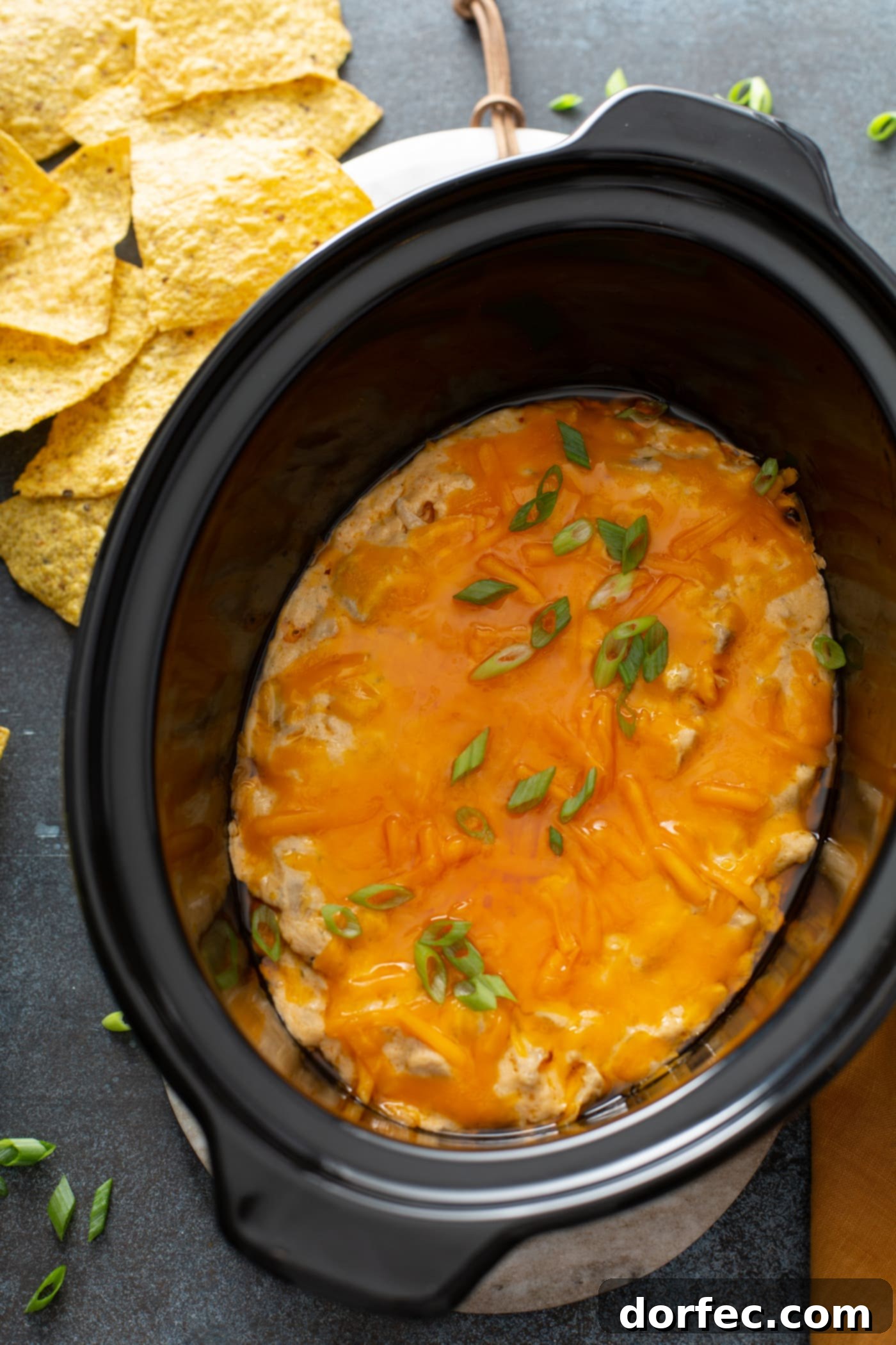 Creamy Buffalo Chicken Dip in Slow Cooker A slow cooker brimming with perfectly cooked buffalo chicken dip, featuring a smooth, creamy texture and a generous layer of glistening melted cheese on top. Tortilla chips are visible in the background, ready to scoop.
