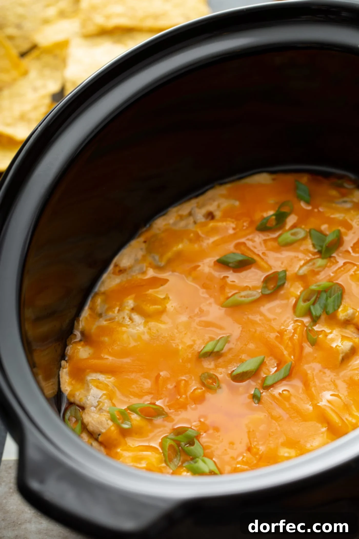 Make-Ahead Buffalo Chicken Dip A slow cooker filled with warm, bubbling buffalo chicken dip, beautifully topped with a layer of melted cheese. A bowl of crispy tortilla chips sits nearby, inviting guests to dig in.