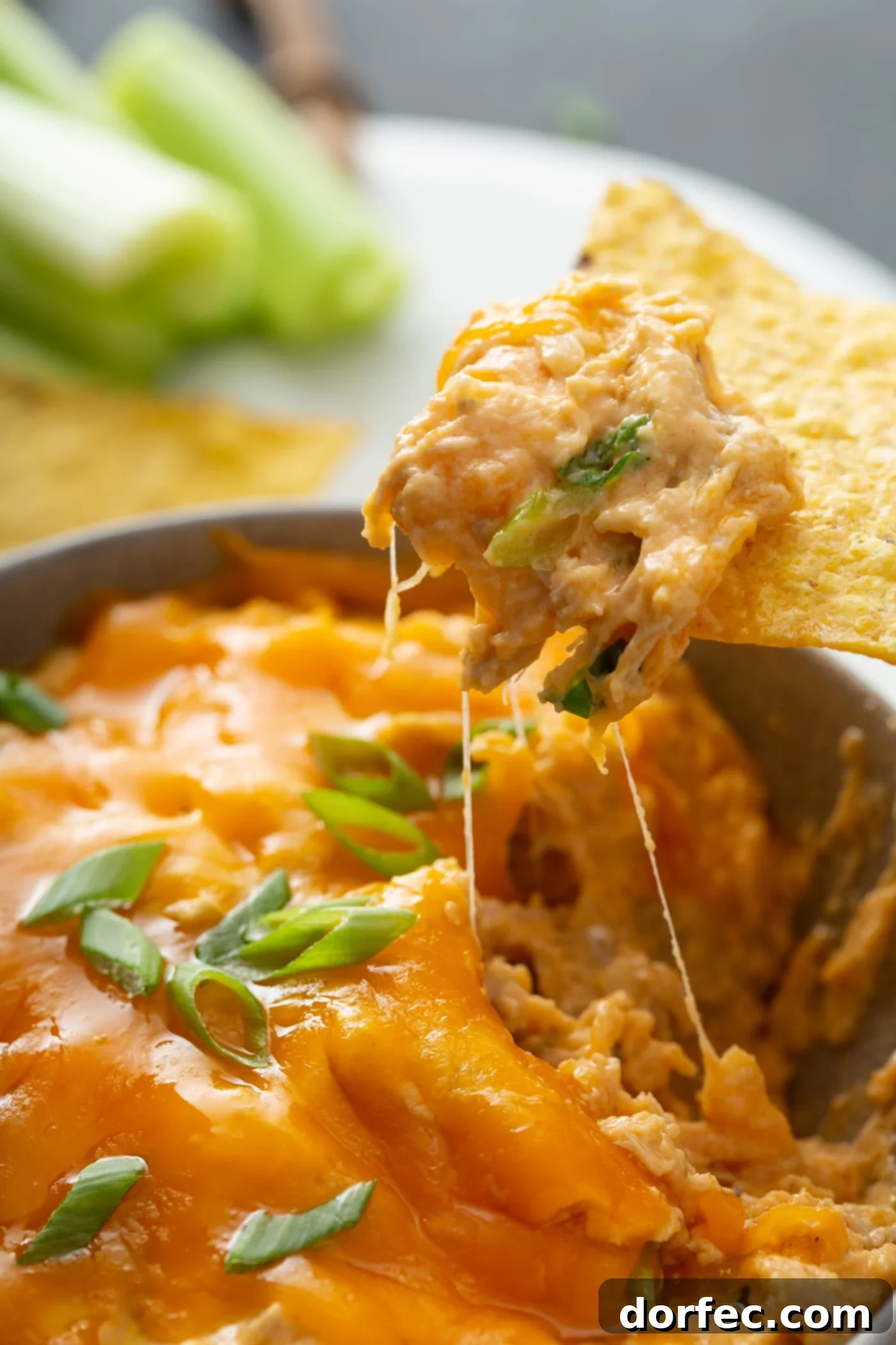 Rich and Creamy Buffalo Chicken Dip A close-up of creamy buffalo chicken dip, with a tortilla chip dipped in, revealing tender shredded chicken bathed in a vibrant orange buffalo sauce, topped with melted cheese and fresh green onions.