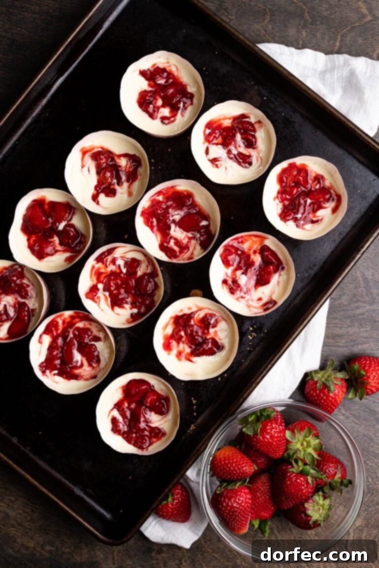 Strawberry Cheesecake Bites 4 Individual muffin cups filled with smooth, creamy cheesecake batter, each featuring a vibrant swirl of strawberry sauce on top.