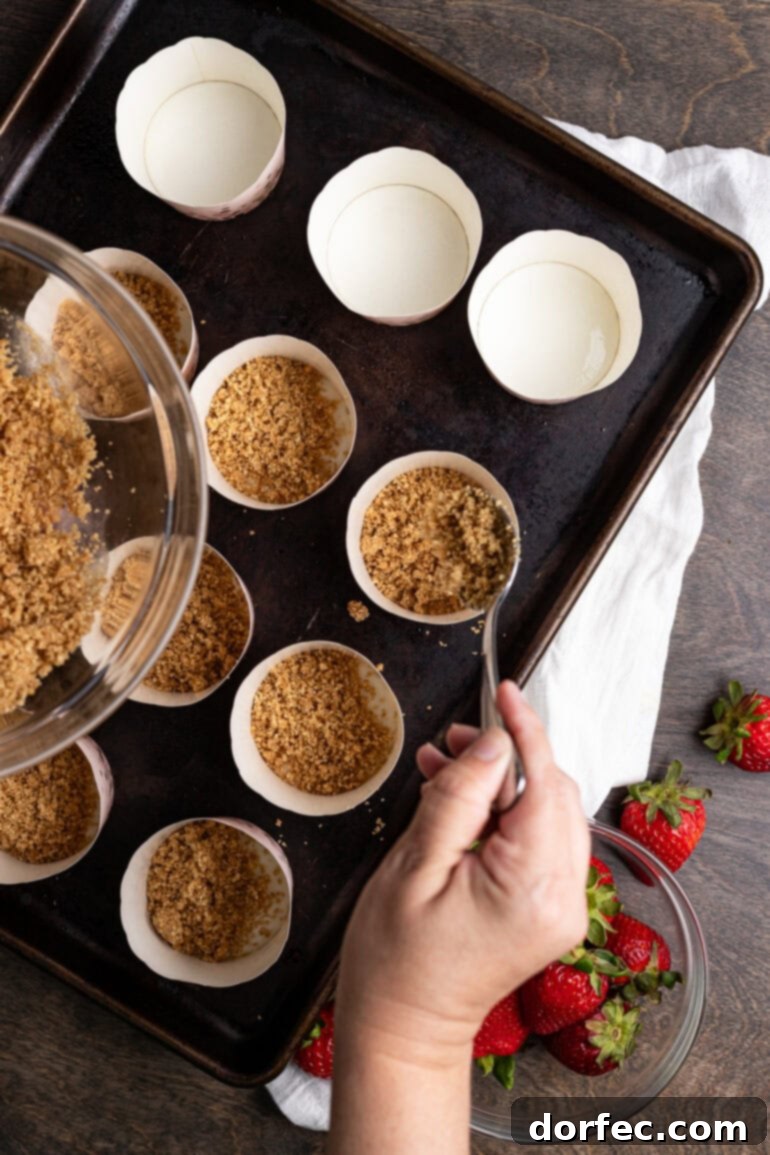 Strawberry Cheesecake Bites 5 A muffin tin with individual paper liners, each containing a perfectly pressed graham cracker crust base, ready for the cheesecake filling.