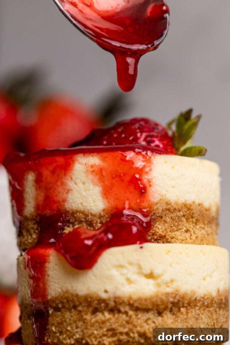 Strawberry Cheesecake Bites 7 A stack of golden mini cheesecakes awaits, while a spoon delicately drips vibrant berry topping over them, creating a cascade of deliciousness.