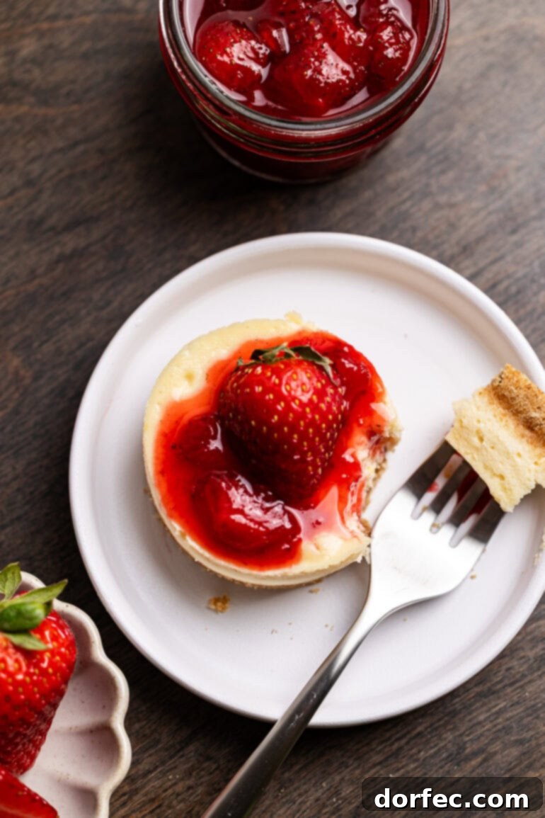 Strawberry Cheesecake Bites 8 A fork is poised to take a delightful bite out of a personal-sized mini strawberry cheesecake, adorned with a generous swirl of berry topping.