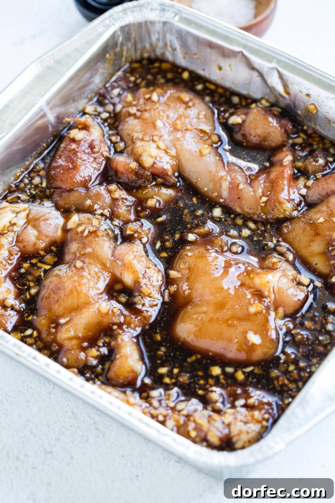 A large dish with chicken thighs marinating in a dark brown sauce.