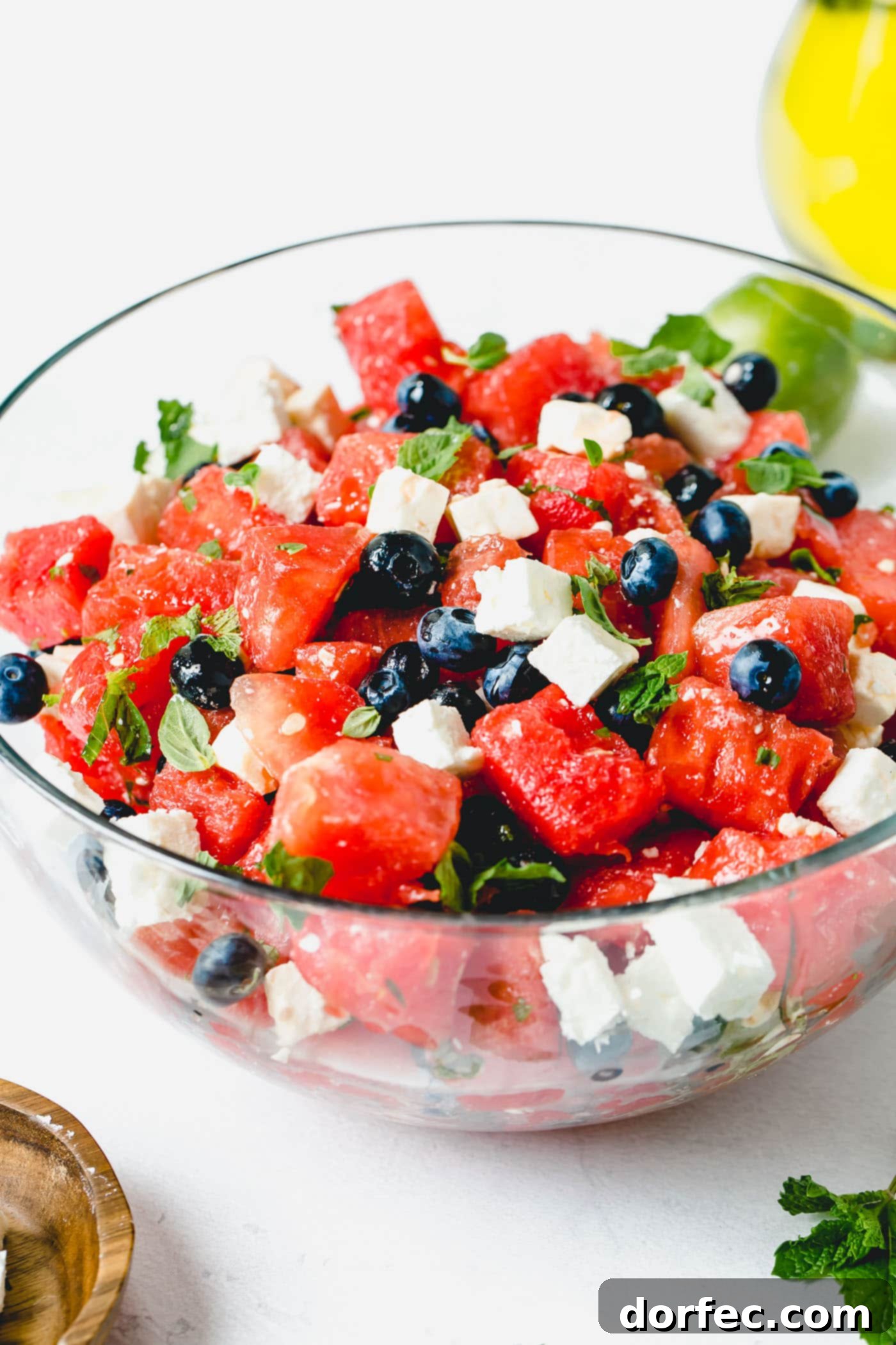 Blueberry Feta Watermelon Salad A vibrant bowl of blueberry feta watermelon salad, featuring crisp watermelon cubes, sweet blueberries, and creamy feta, garnished generously with fresh basil and mint leaves.