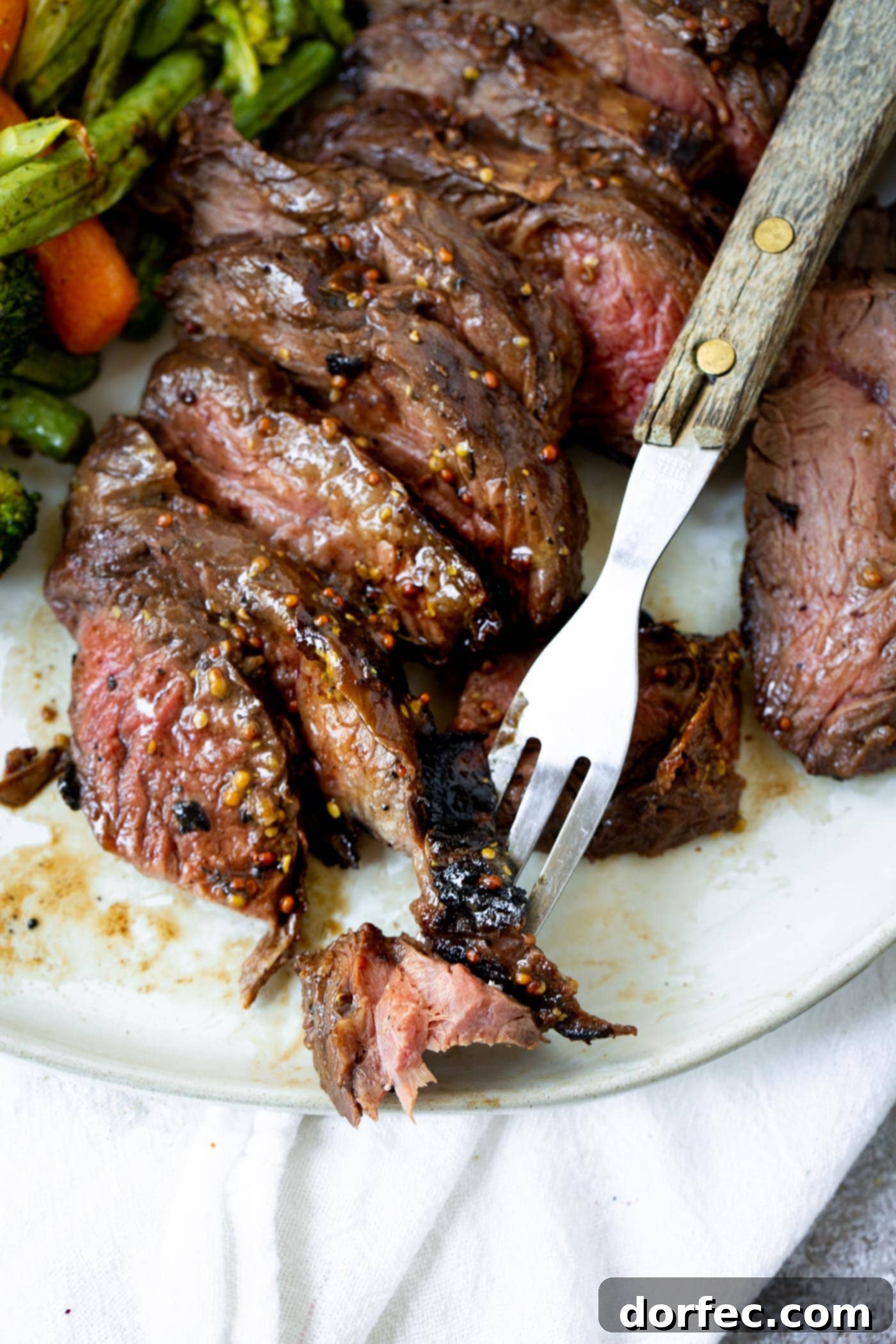 A photo of a fork picking up one piece of sliced medium rare hanger steak.