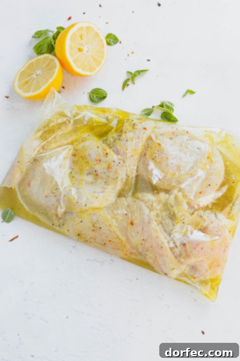 Four chicken breasts immersed in a golden-brown marinade inside a ziplock bag, with fresh lemon slices visible in the background, signaling freshness.