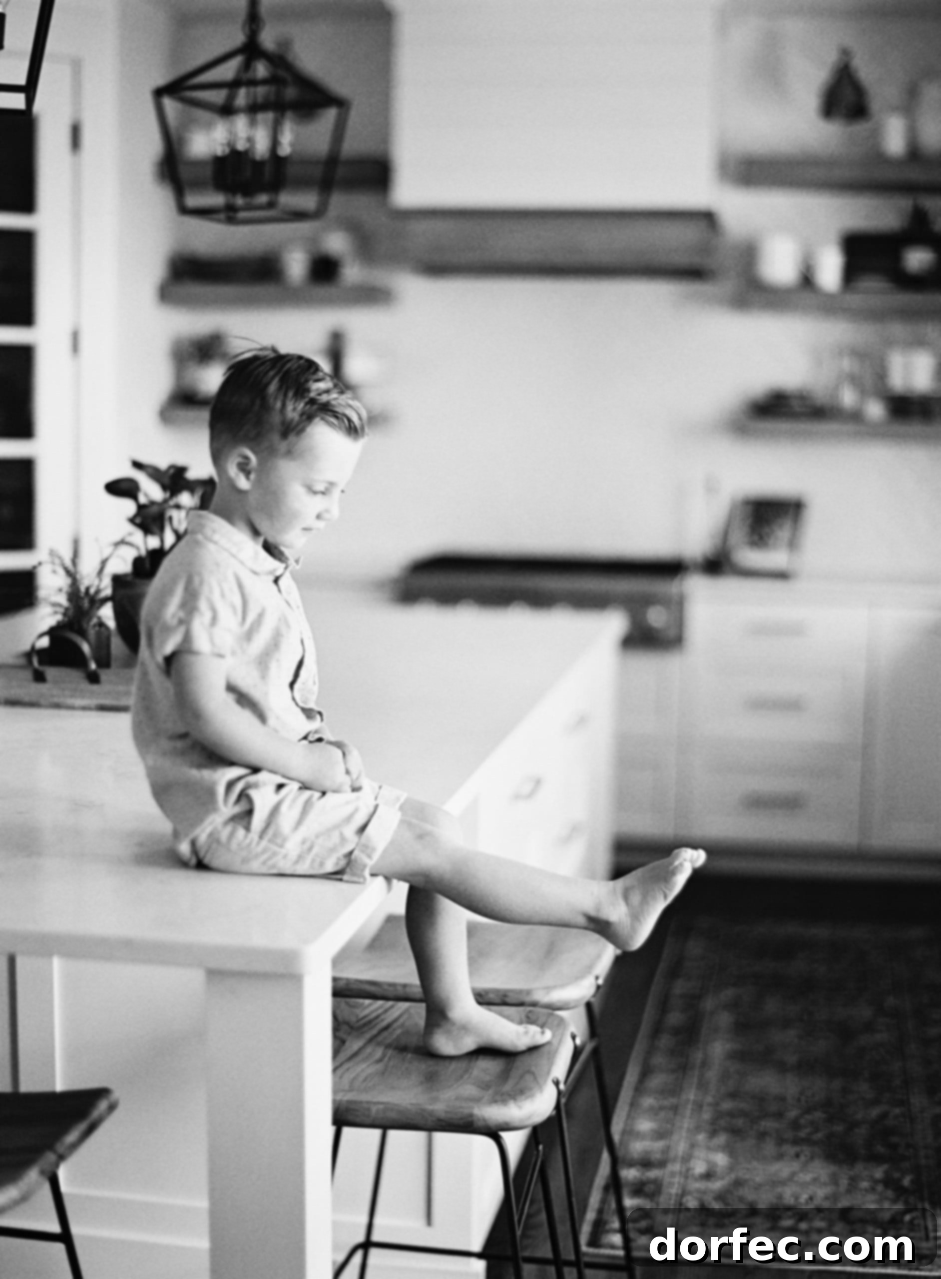 A young boy sits on a counter, thoughtfully looking at his toes, embodying the innocence and introspection of childhood.