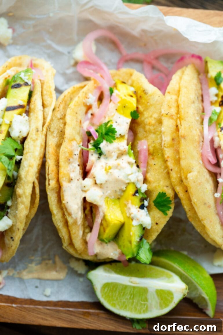 Smoky Grilled Avocado Tacos 4 A photo taken above three grilled avocado tacos in grilled corn tortillas topped with pickled onions, lime crema and crumbled queso fresco.