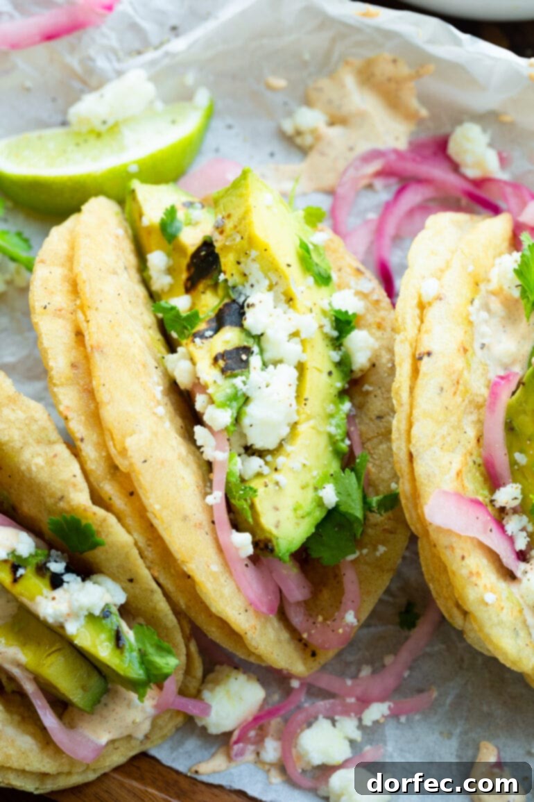Smoky Grilled Avocado Tacos 8 A close-up photo of a grilled avocado taco topped with crumbled queso fresco and pickled onions in grilled corn tortillas.