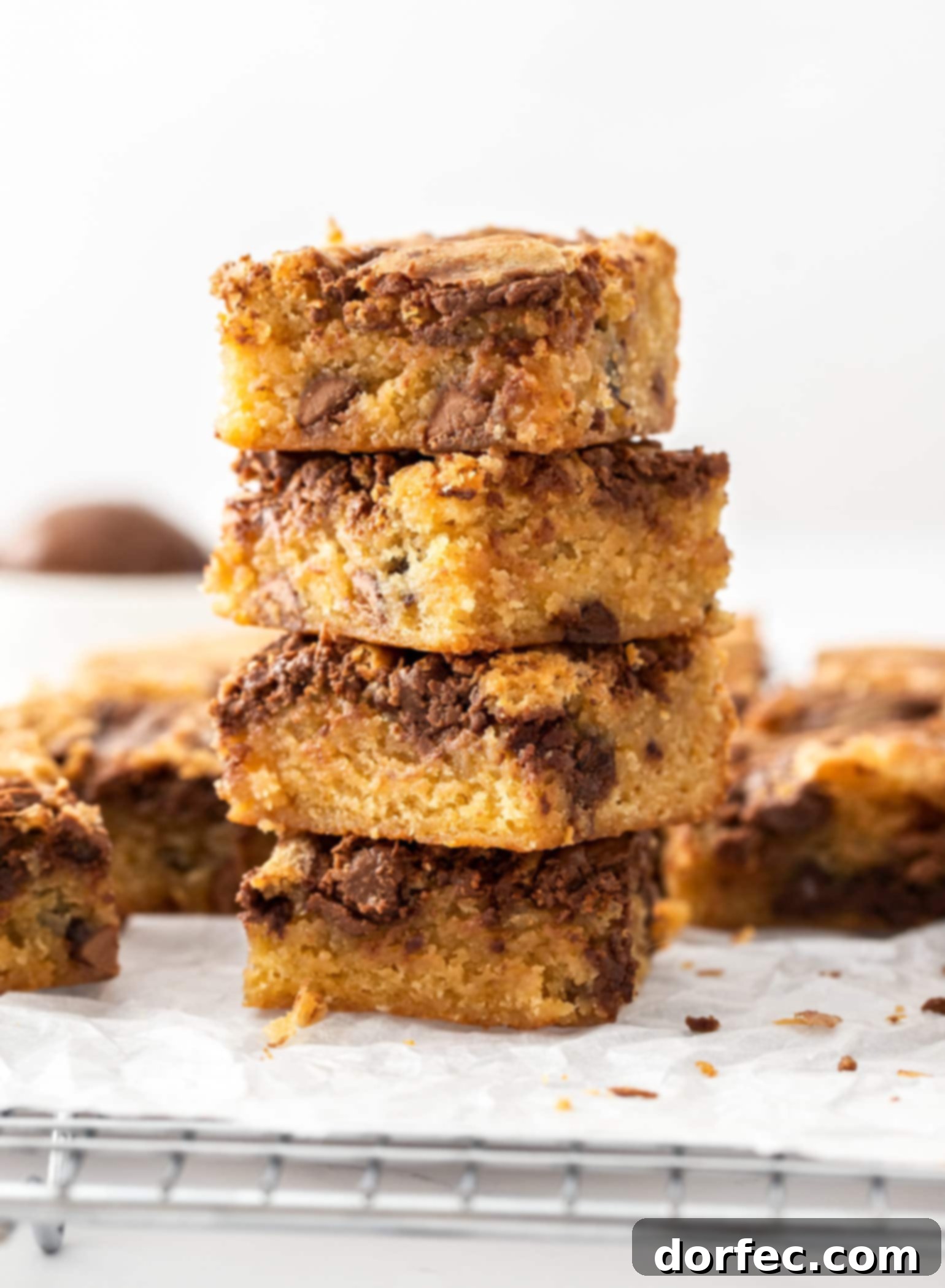 A stack of 4 blondie bars sitting on a wire rack with more around them, highlighting their soft and chewy texture.