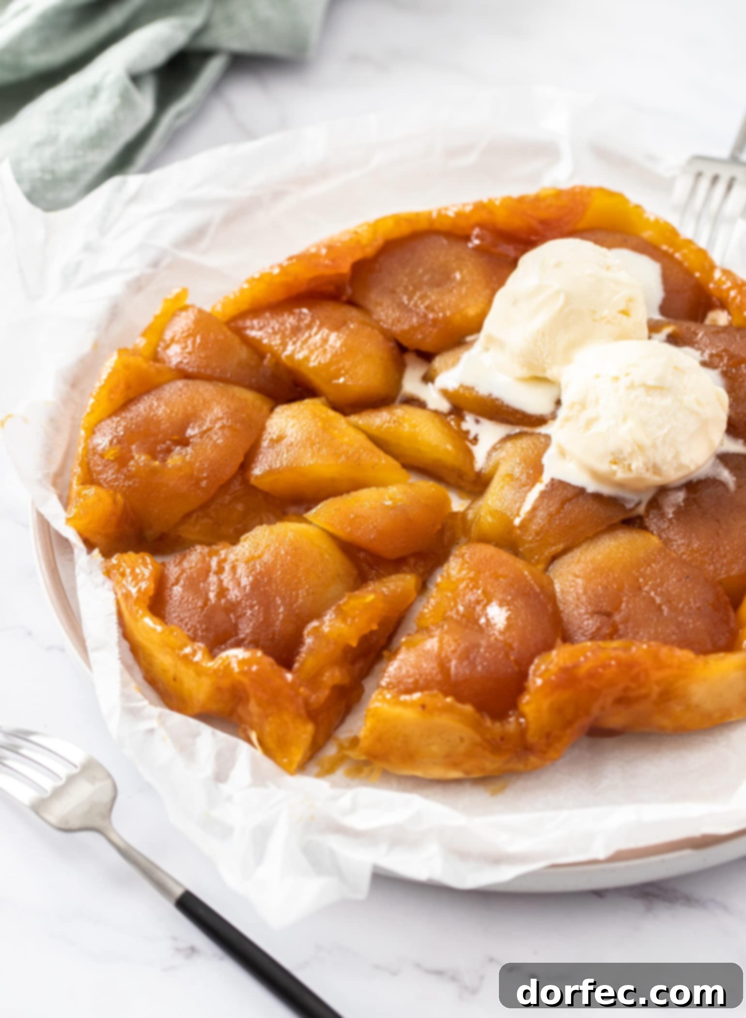 Caramelized Apple Tarte Tatin 6 A freshly baked Apple Tarte Tatin on a sheet of baking paper on a marble counter, adorned with a melting scoop of vanilla ice cream, showcasing its golden crust and caramelized apples.