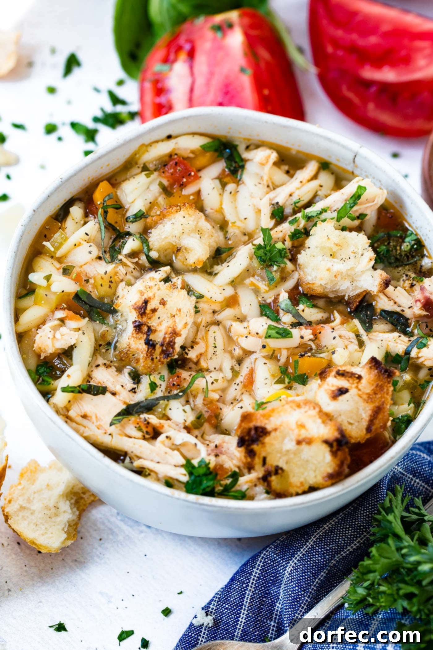 A large white soup bowl brimming with Instant Pot Italian Chicken Soup, featuring visible orzo pasta, shredded chicken, and fresh parsley, garnished with crusty bread.