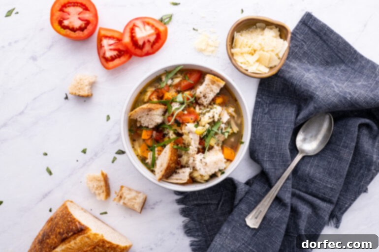 A large bowl of Instant Pot Italian Chicken Soup on a table, accompanied by a silver spoon, quartered Roma tomatoes, and crusty bread slices.
