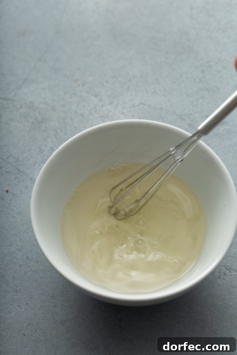 Foolproof Stabilized Whipped Cream 3 A white mixing bowl with a whisk attachment, showcasing partially whipped cream that is starting to thicken into soft peaks.