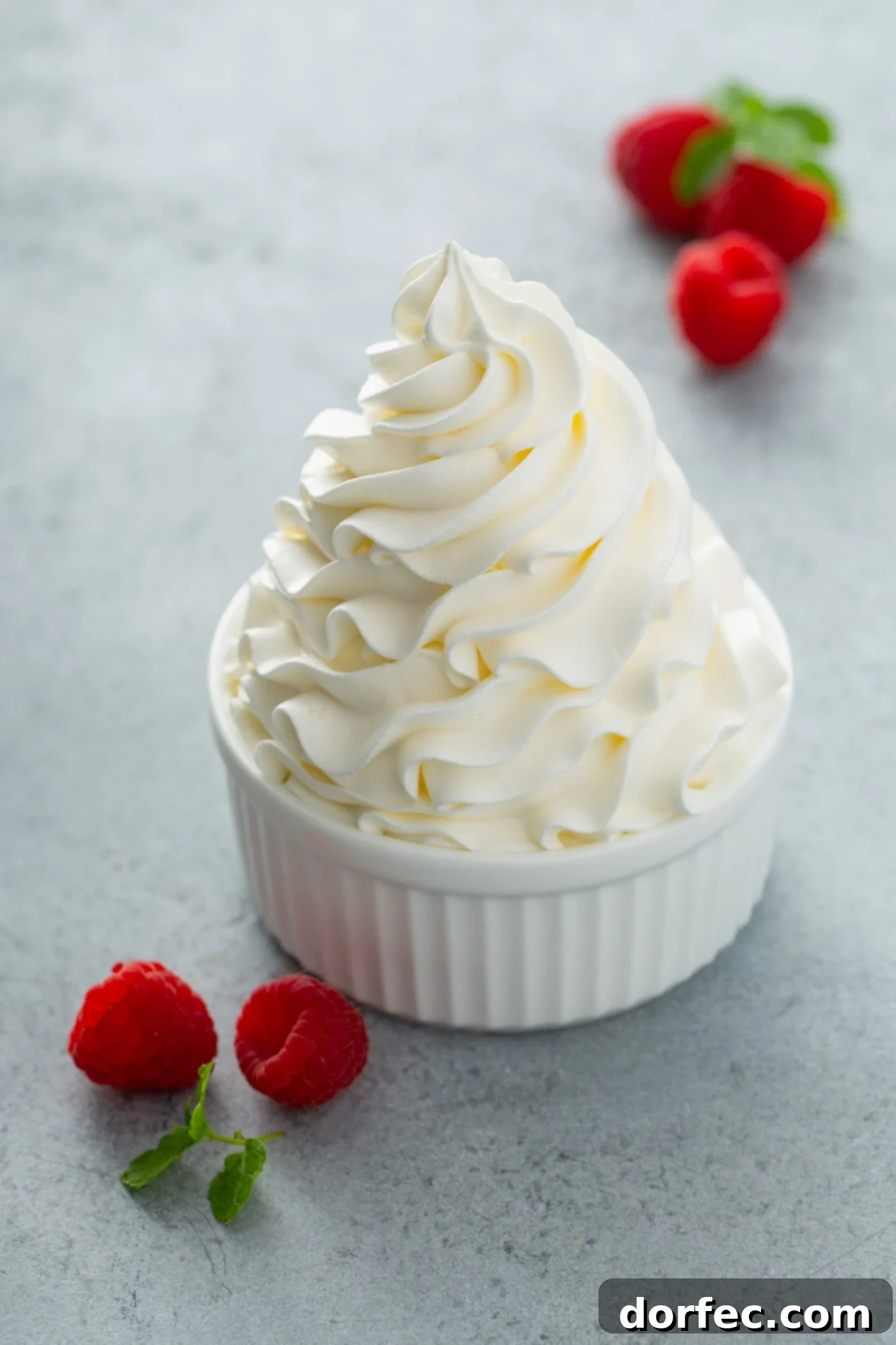 Versatile Stabilized Whipped Cream A perfectly swirled peak of stabilized whipped cream presented in a glass bowl, with a scattering of fresh raspberries around it. The cream appears incredibly rich and fluffy.