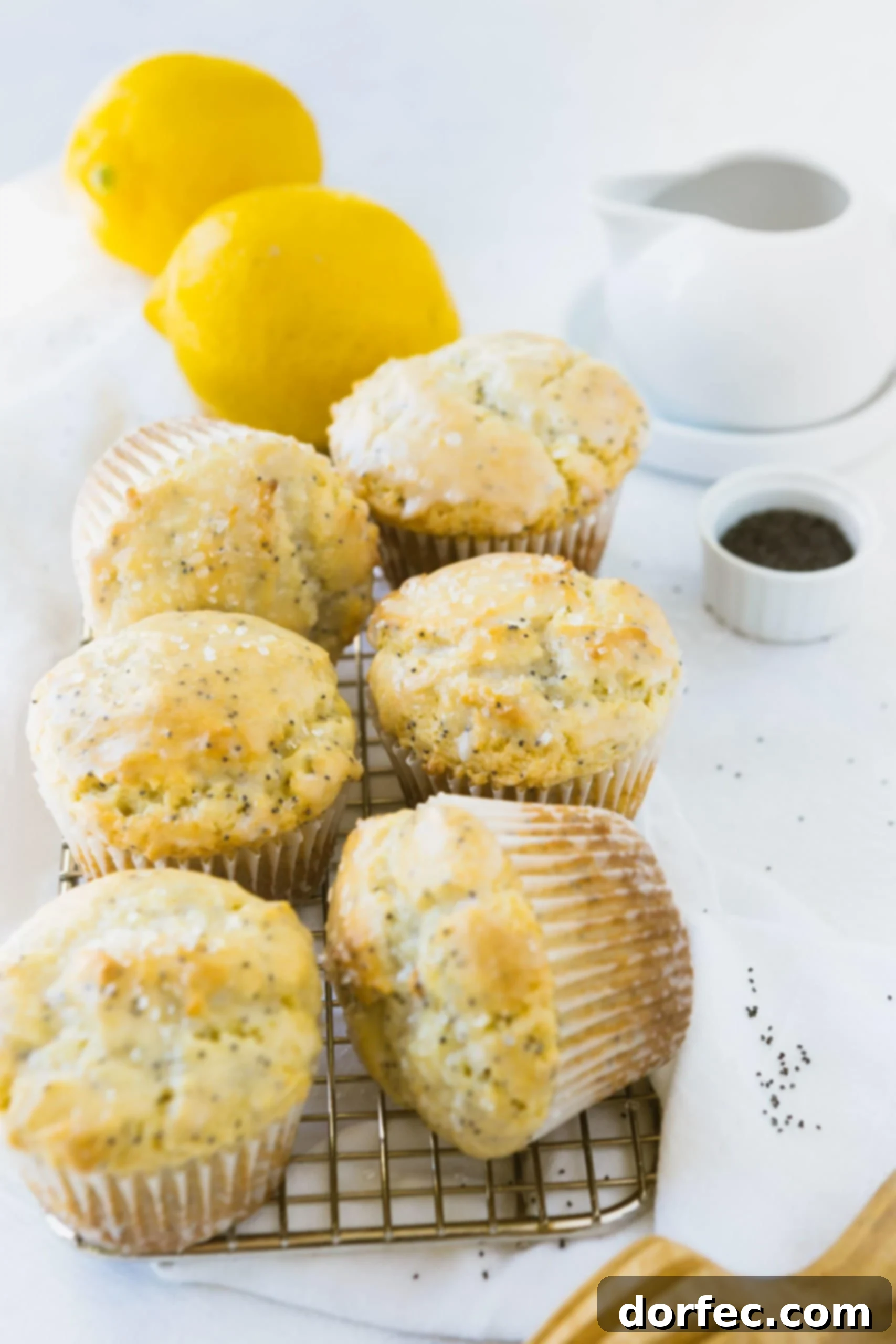 Zesty Lemon Poppy Seed Muffins 2 Six perfectly baked lemon poppy seed muffins, generously drizzled with a glistening lemon glaze. Two fresh lemons rest in the soft-focus background, hinting at the vibrant citrus flavor within.