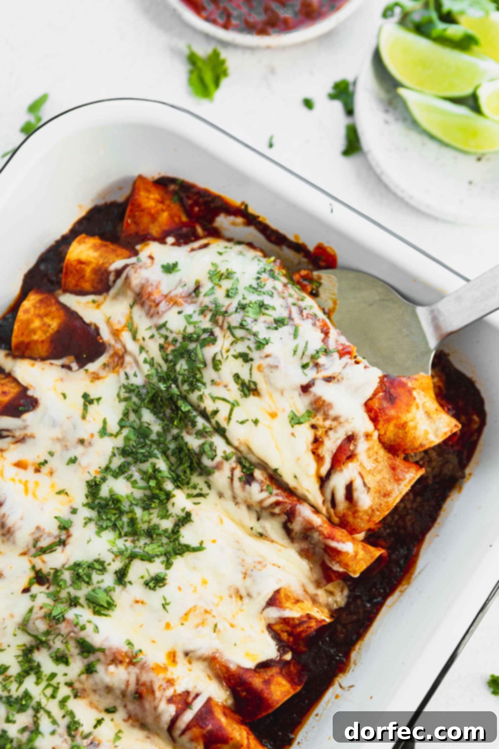 A photo of a pan of ground beef enchiladas with the first two being removed with a metal spatula.
