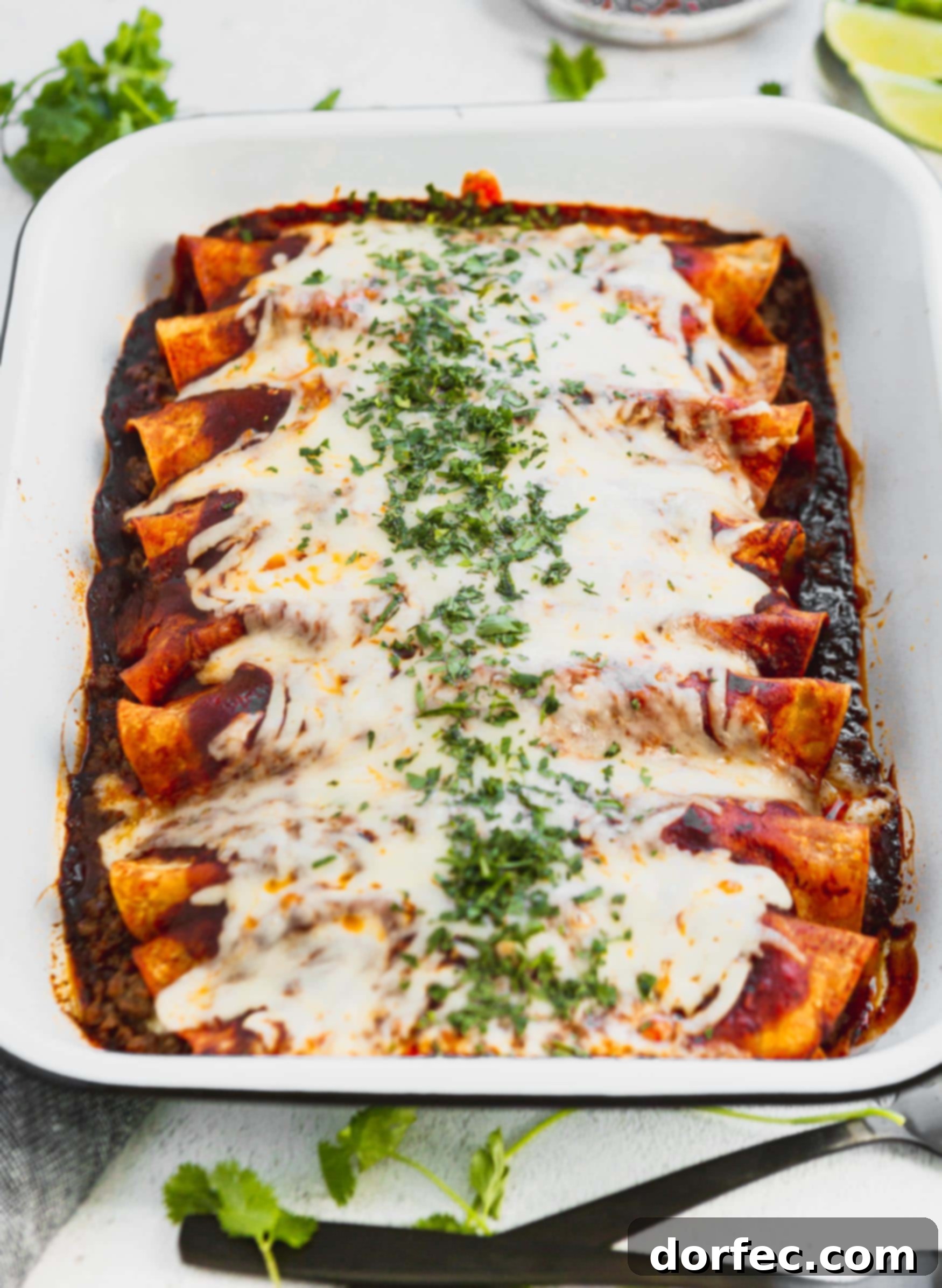 A photo of a pan of ground beef enchiladas covered in melted cheese and finely chopped cilantro.