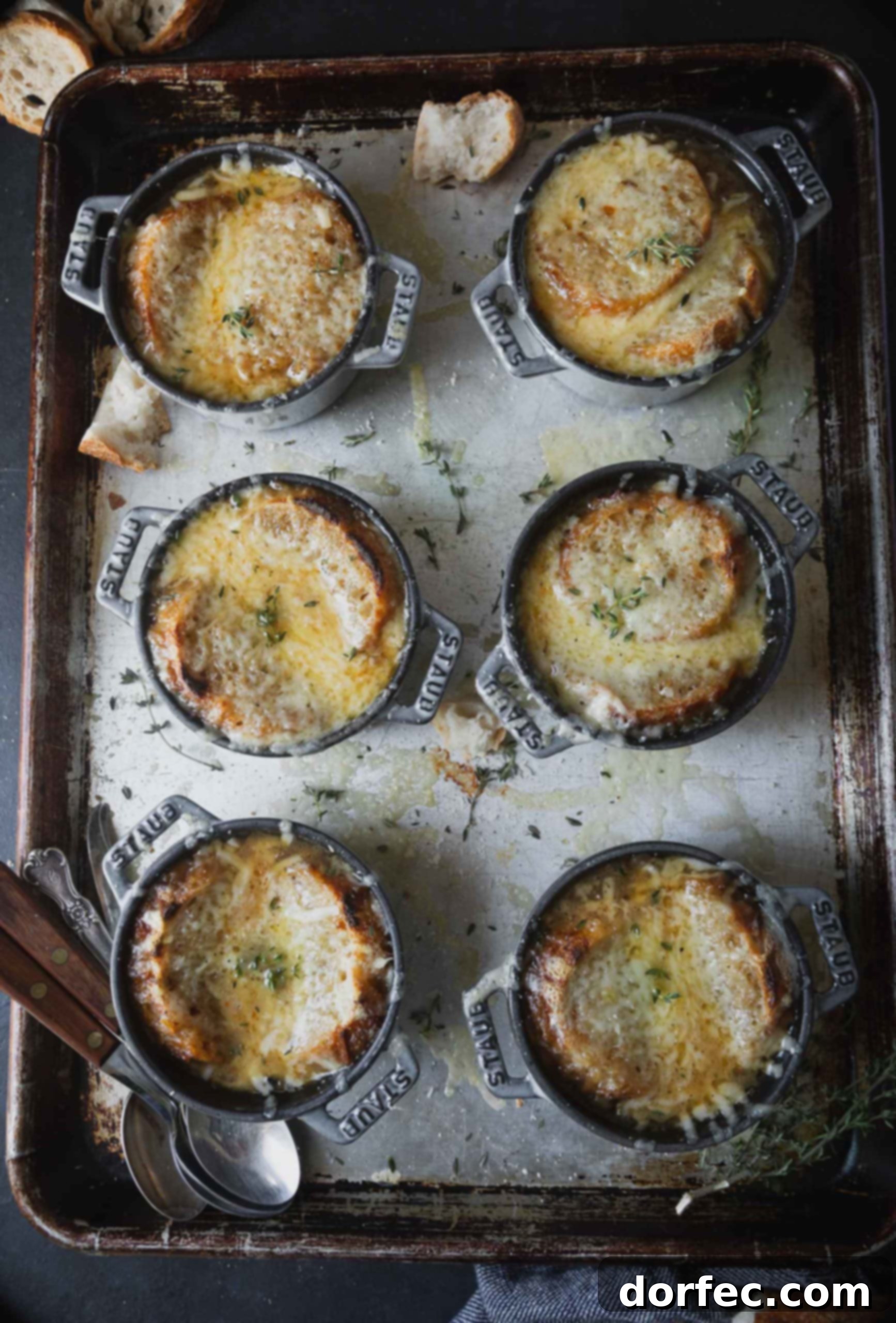 A baking sheet with containers of Onion soup. The soup has a bread and cheese topping that has been toasted in the oven.