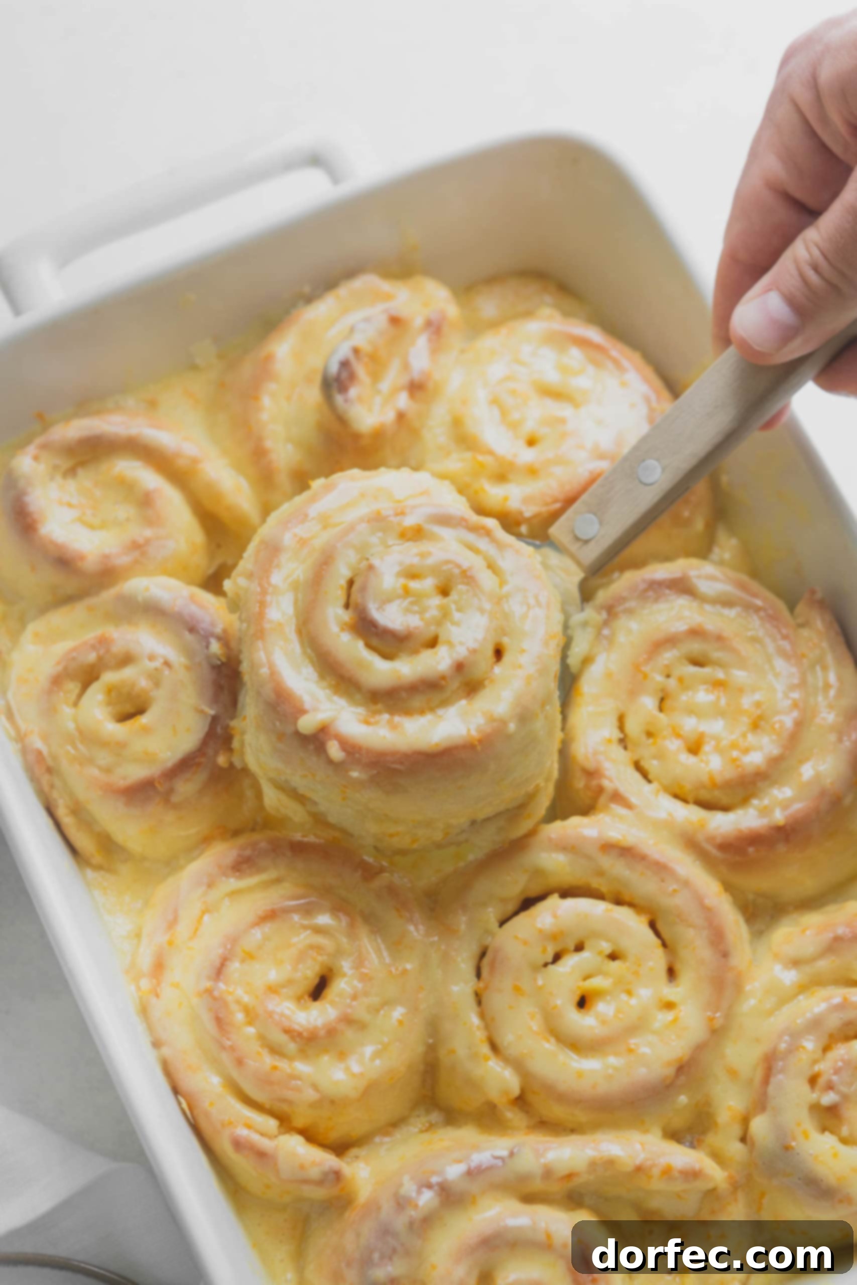 Orange Rolls An orange roll being lifted from a pan of freshly baked orange rolls. The rolls are frosted with an orange glaze.
