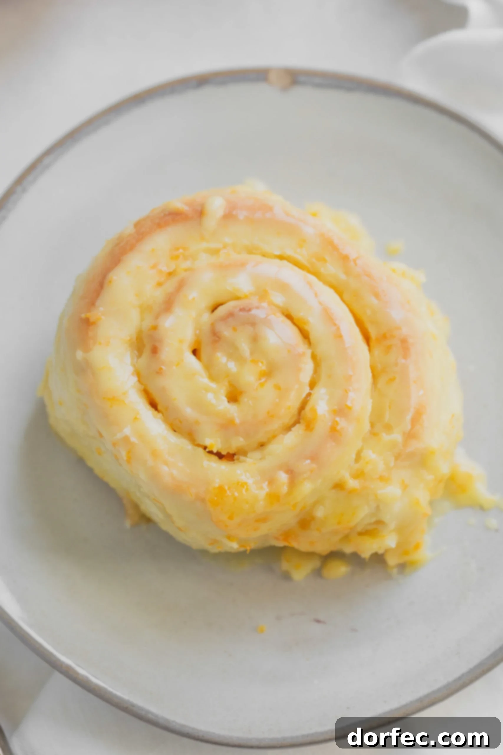 Orange Rolls An orange roll on a white plate. The roll is soft and fluffy and frosted with an orange glaze with bits of orange zest.