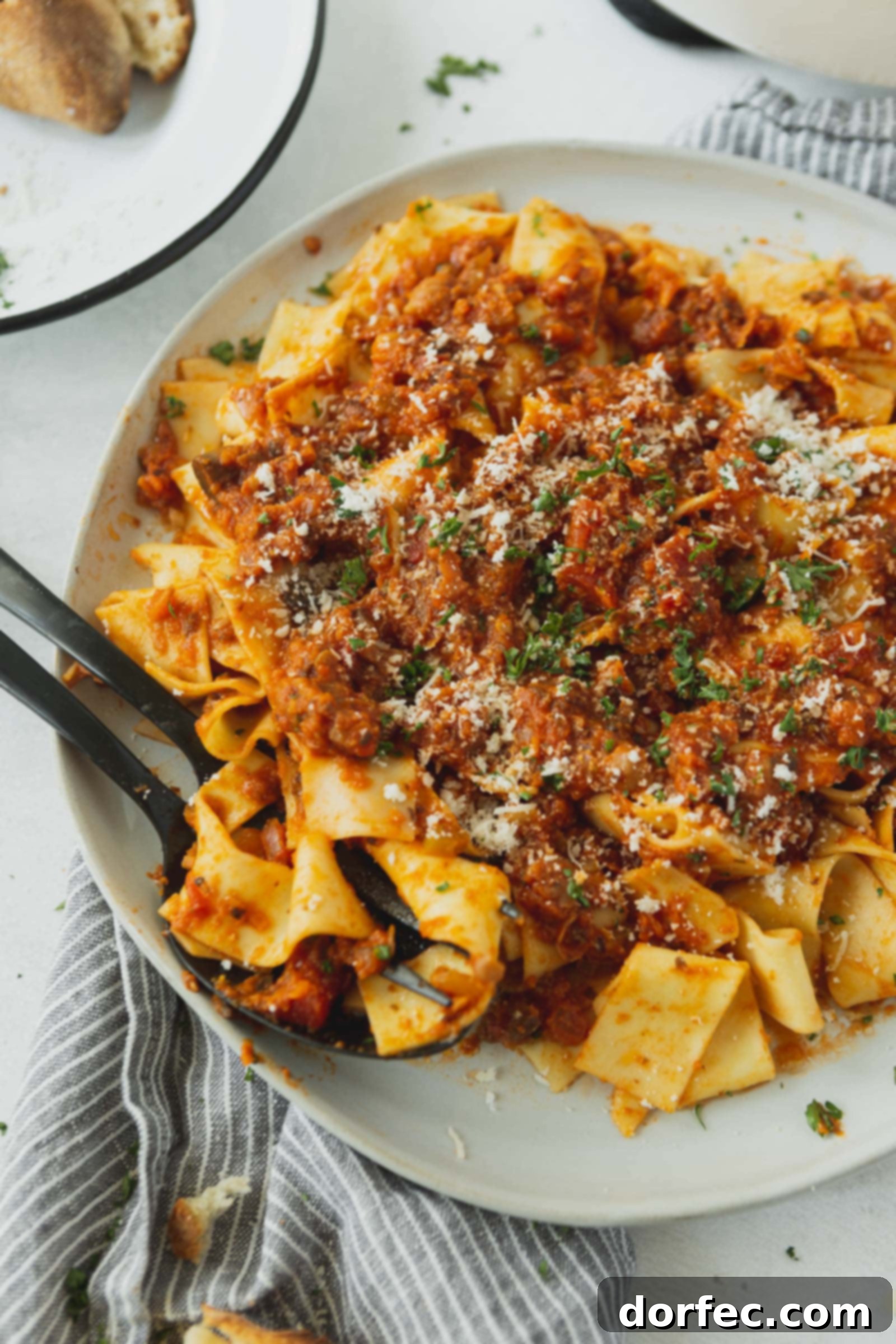 A serving plate of pasta with a thick, vibrant vegan bolognese sauce, topped with grated cheese and fresh cilantro.