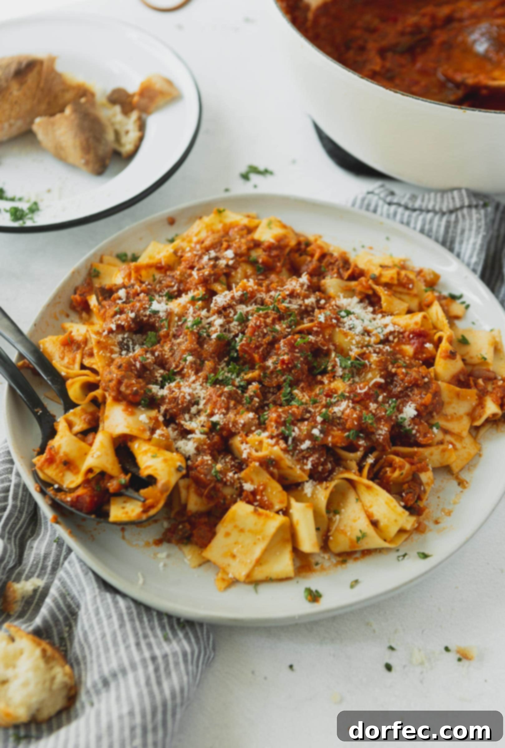 A plate full of pasta topped with vegan bolognese sauce. There is a fork on the plate and the pasta is topped with a little grated cheese and cilantro.