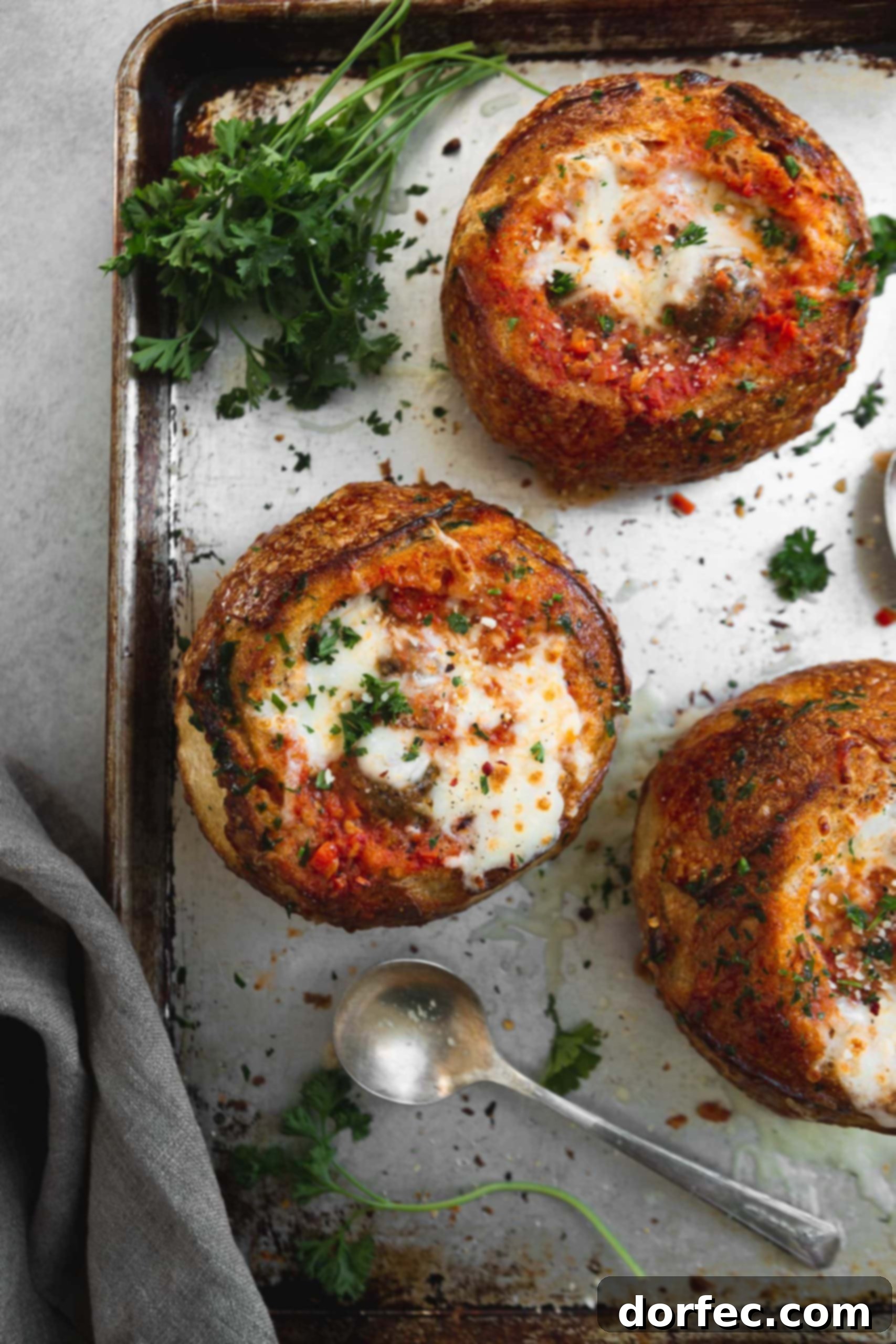 Parmesan Meatball Soup A baking sheet with three bread bowls filled with parmesan meatball soup. They have been baked to a golden brown and the cheese on top is melted to perfection. They are sprinkled with fresh parsley.