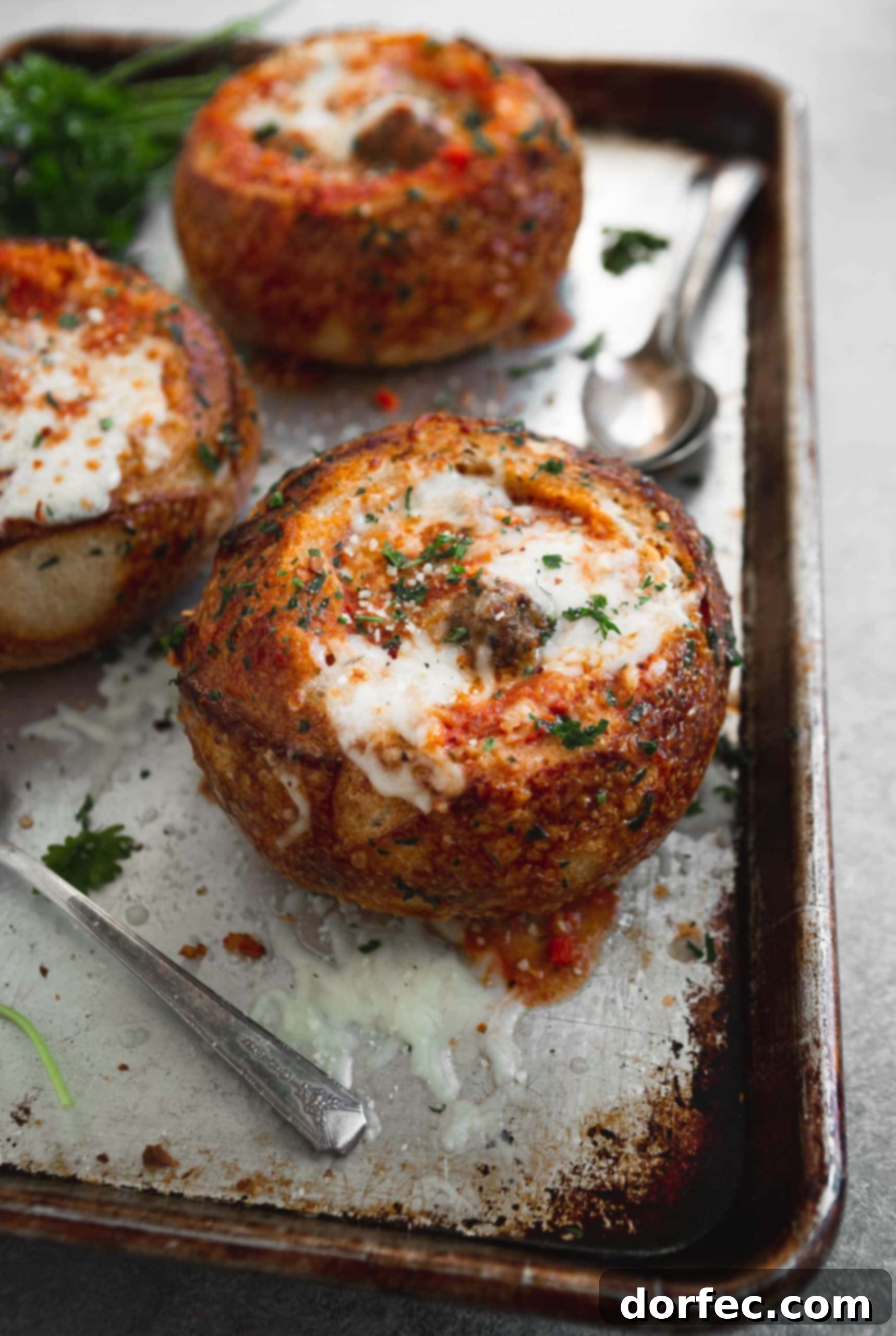 Parmesan Meatball Soup Three toasted bread bowls filled with meatball parmesan soup. There is melted cheese sprinkled with fresh parsley on top.