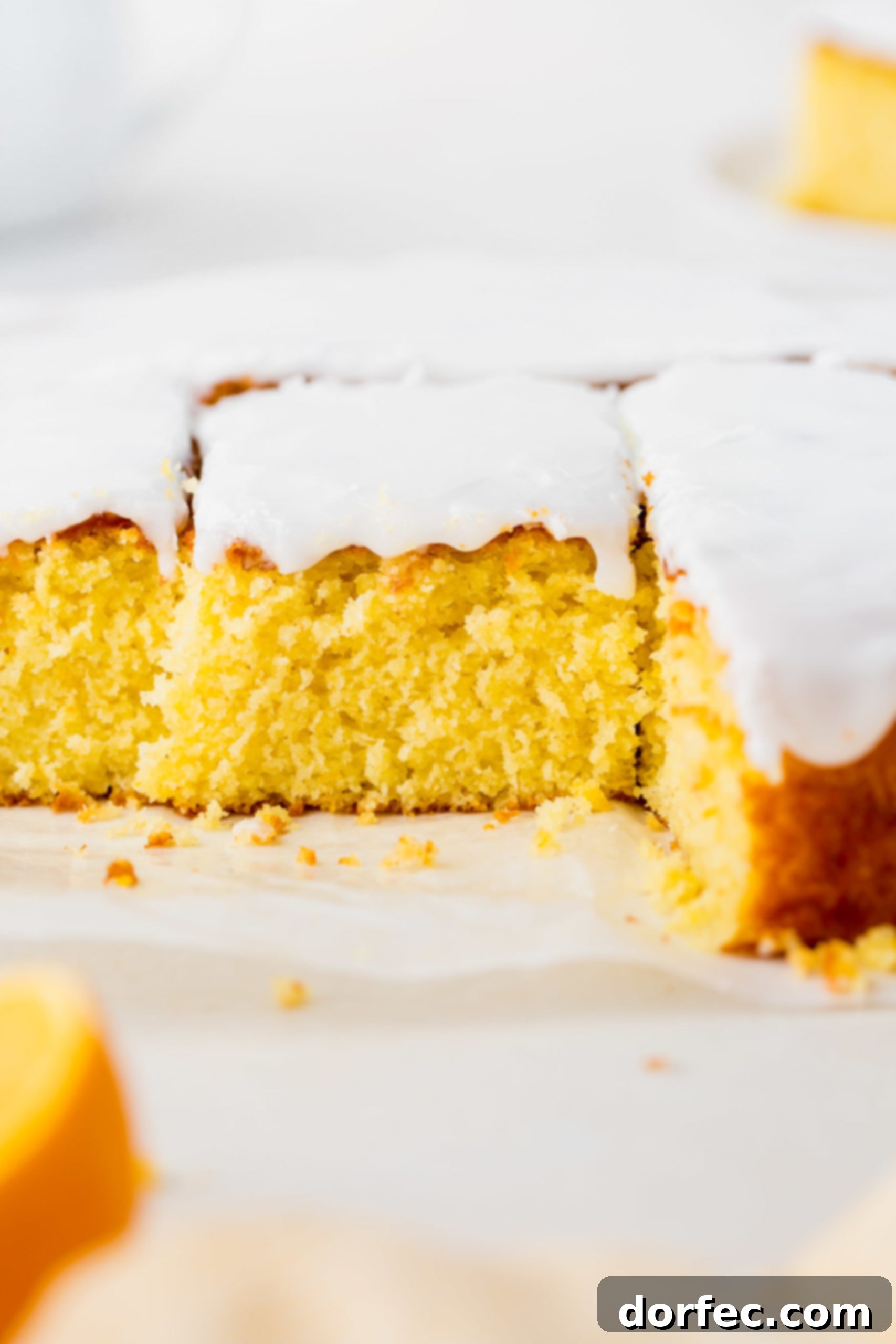 A lemon cake covered in white frosting with some pieces removed. The middle piece is cut but not yet removed.