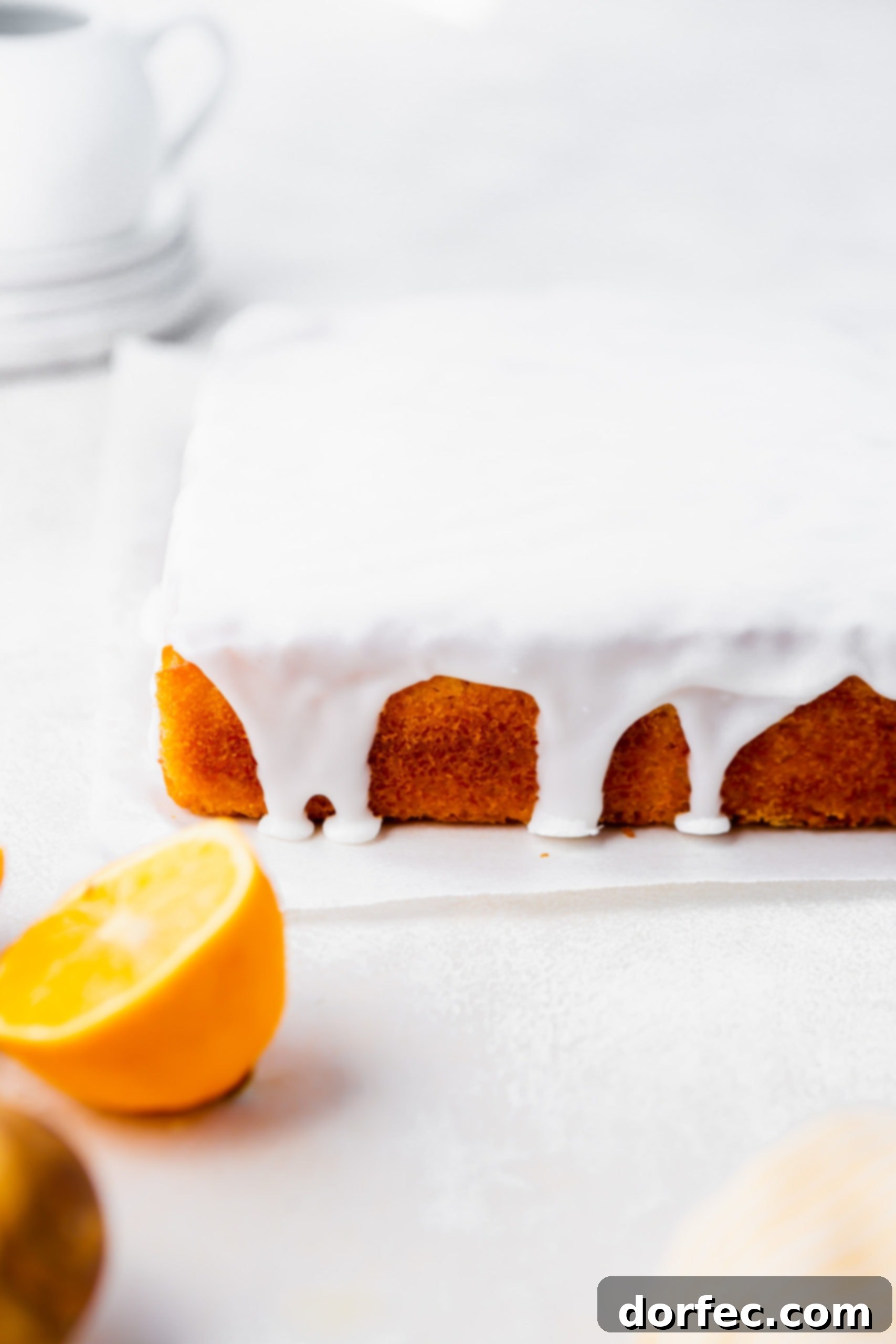A square lemon cake covered in a white lemon glaze dripping down the sides.