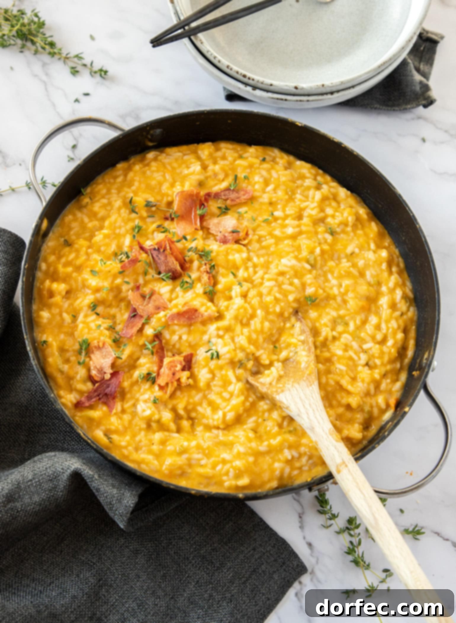 Creamy Sweet Potato Risotto 4 A large skillet brimming with vibrant orange sweet potato risotto, surrounded by fresh herbs and small serving bowls.
