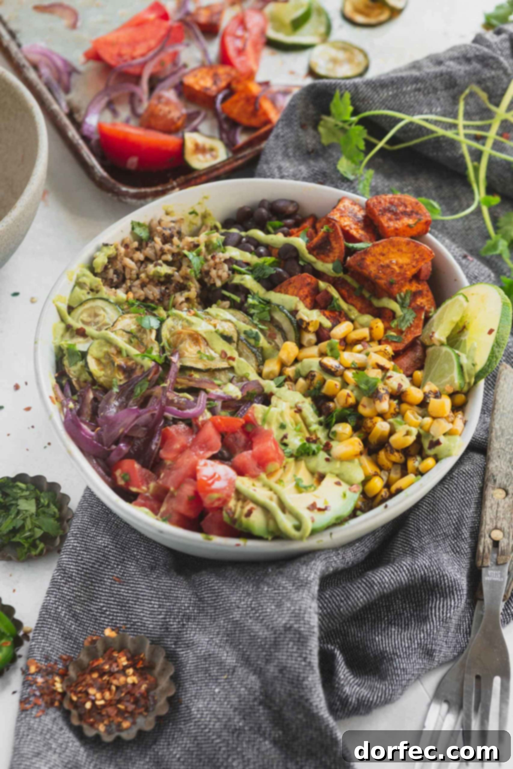 Hearty and Flavorful Plant Powered Burrito Bowls 2 A vegan burrito bowl that contains tomatoes, avocados, roasted corn, sweet potatoes, zucchini and red onion. There is brown rice and quinoa in the burrito bowl.