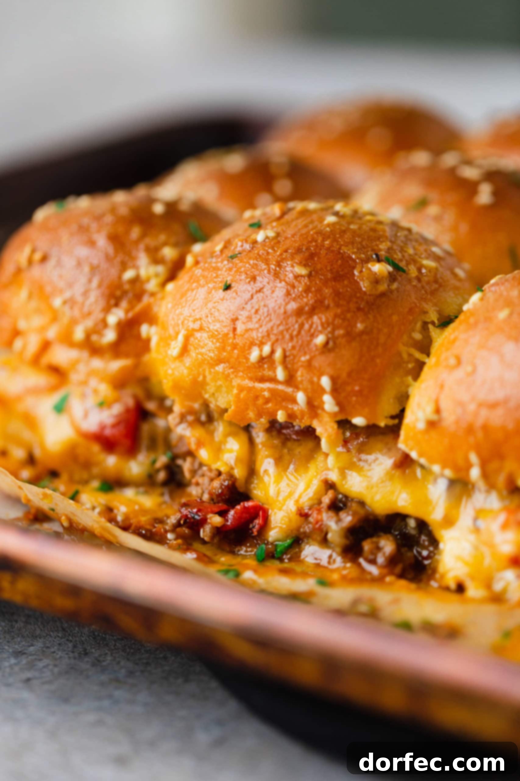 A plate of cheeseburger sliders with melted cheese oozing out from the buns.