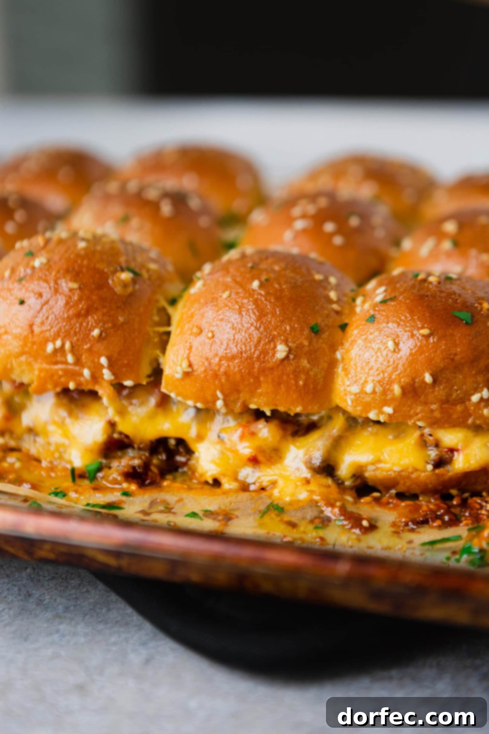 A pan of cheeseburger sliders with hamburger, melted cheese, and golden dinner rolls.