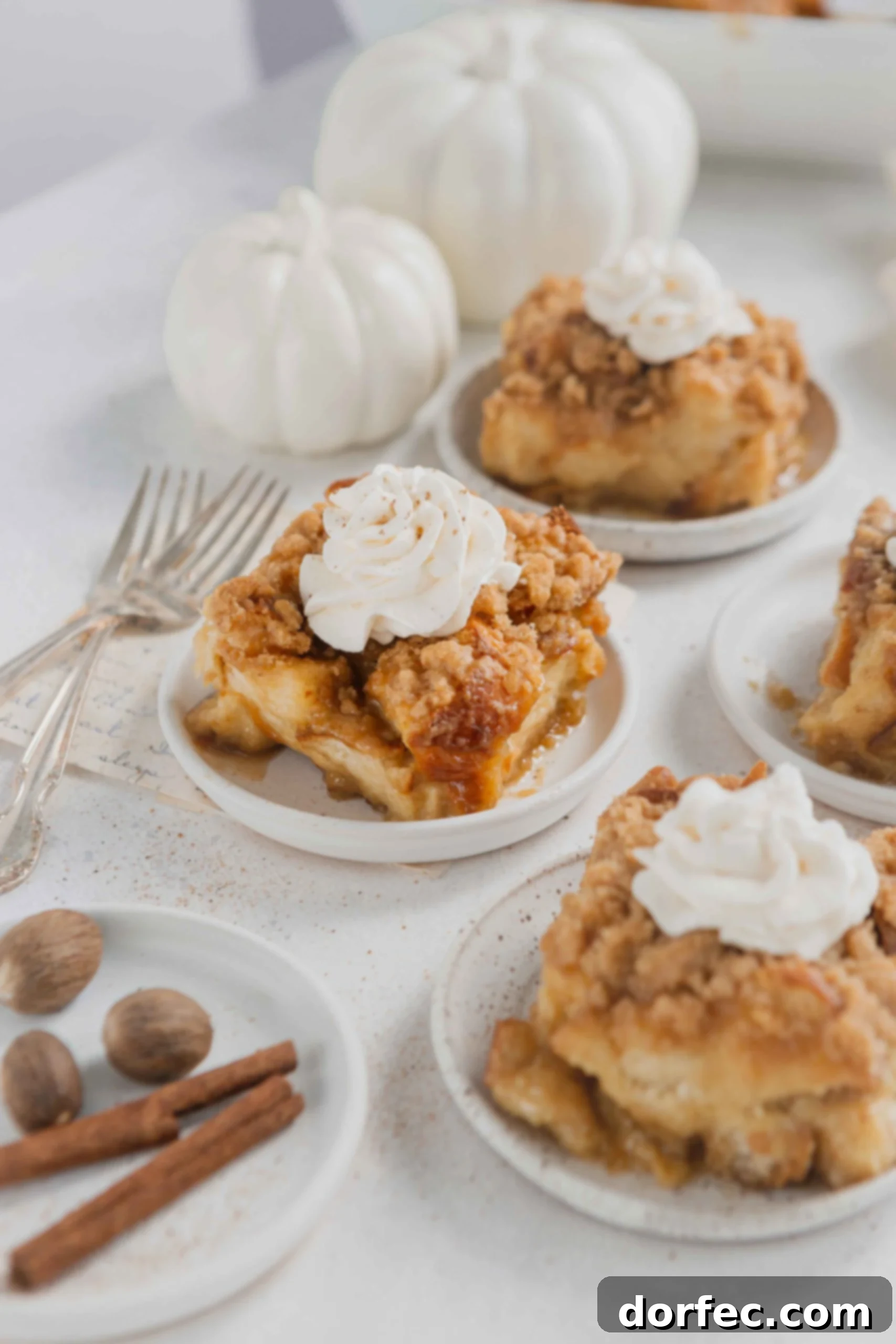 Servings of eggnog French toast casserole on white plates. The casserole is topped with a dollop of fresh whipped cream.