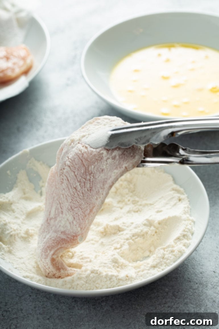 Authentic Southern Crispy Fried Chicken 9 A chicken breast held with tongs, being dredged in eggs and flour.