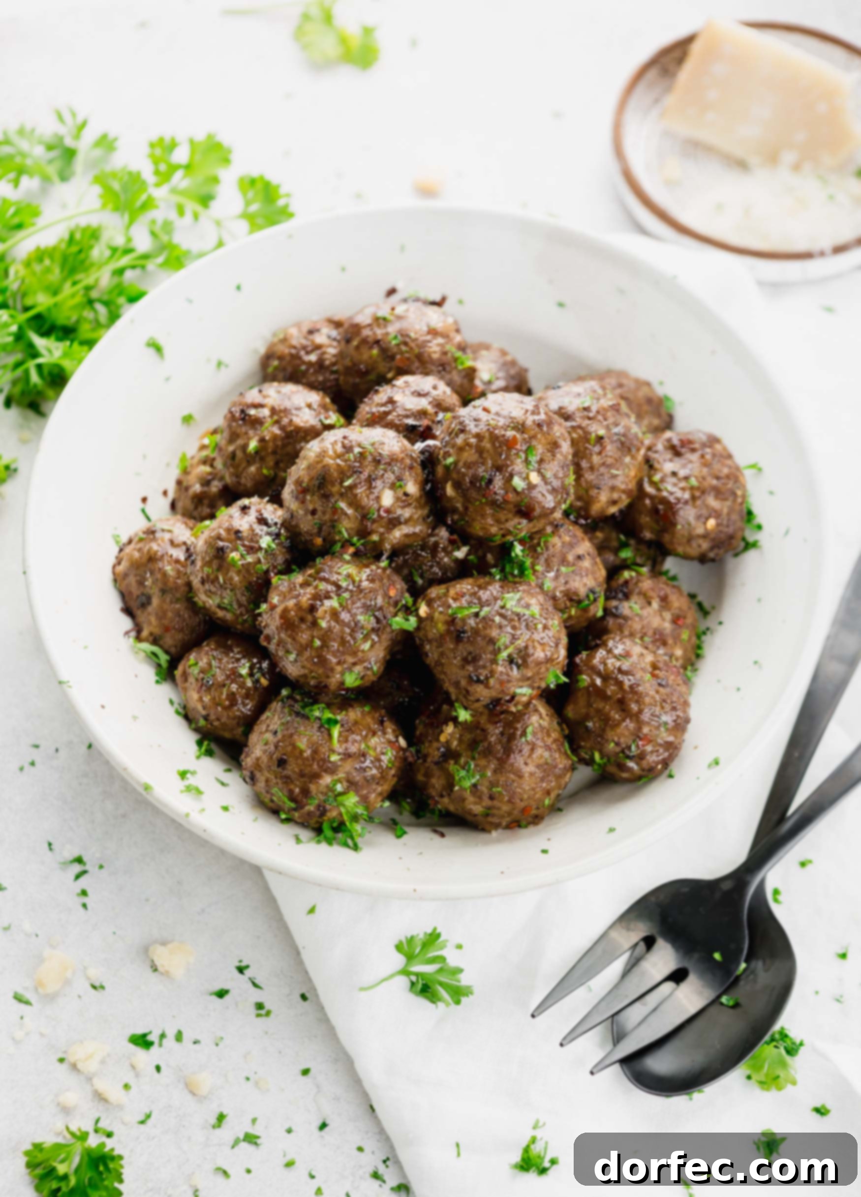 A bowl of perfectly browned meatballs, lightly sprinkled with fresh chopped basil. Two forks are placed alongside the bowl.