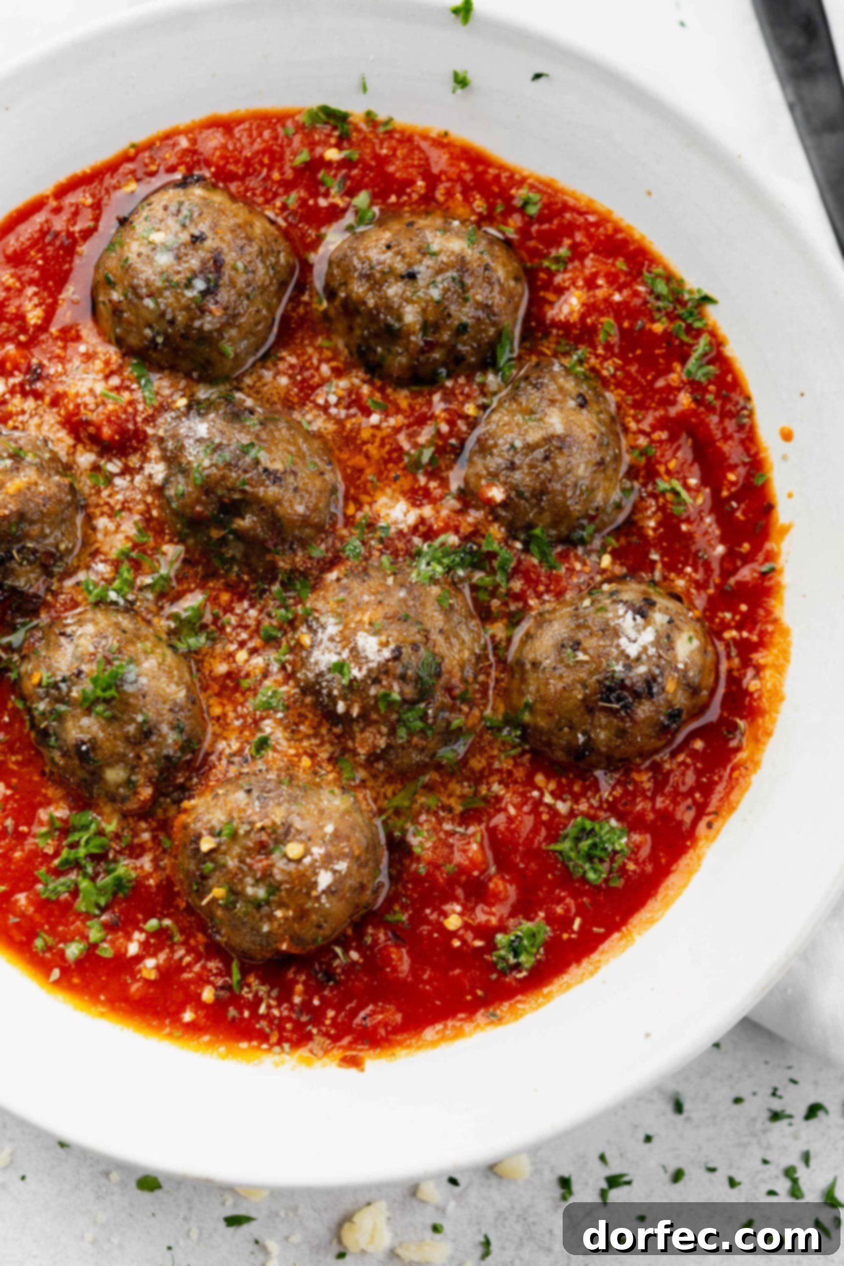 A full bowl of tender meatballs submerged in a rich, flavorful tomato sauce, finished with a fresh parsley garnish.