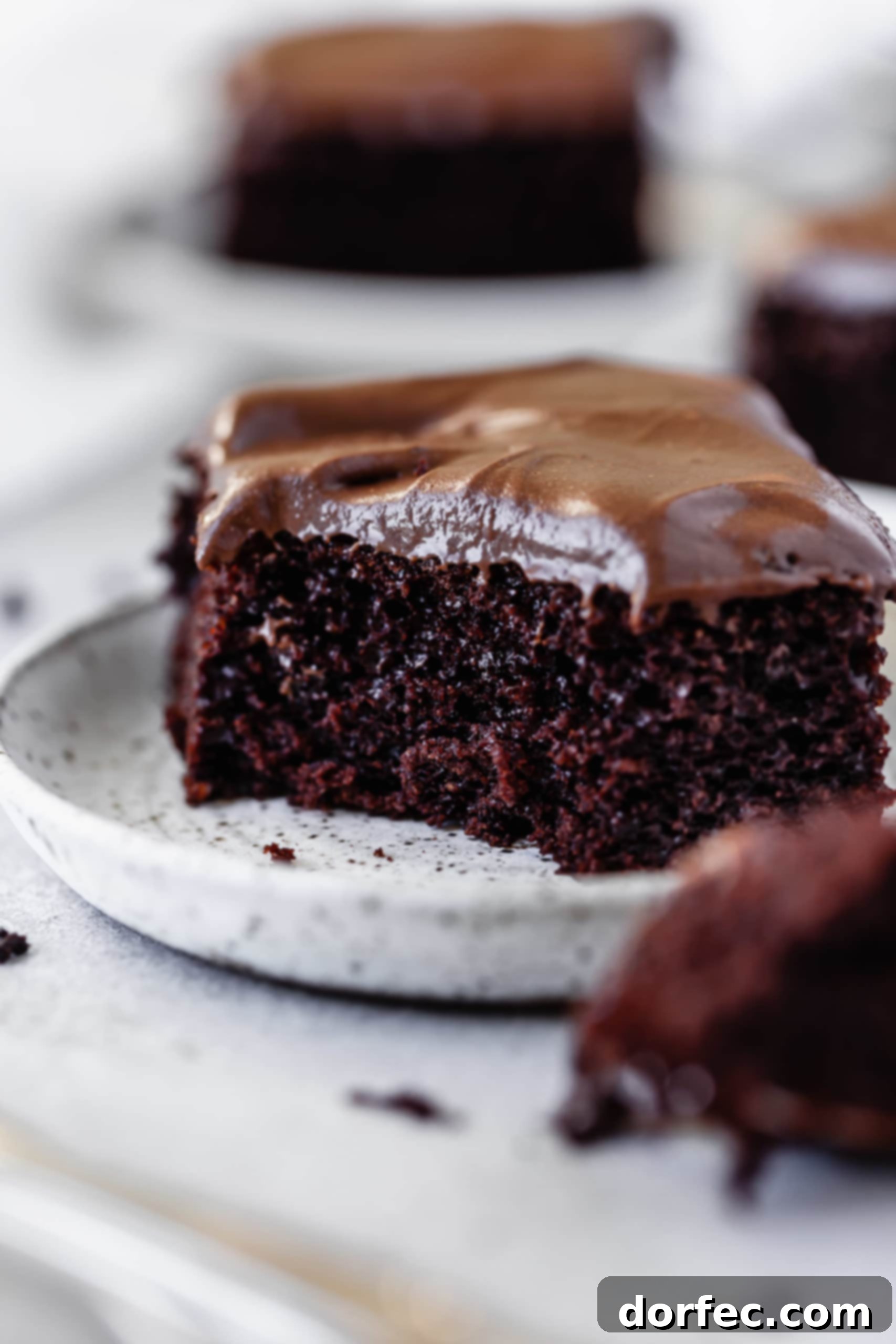 Chocolate Mayonnaise Cake A close-up of a slice of chocolate mayonnaise cake with a fork holding a bite-sized piece, revealing its soft texture and creamy chocolate cream cheese frosting.
