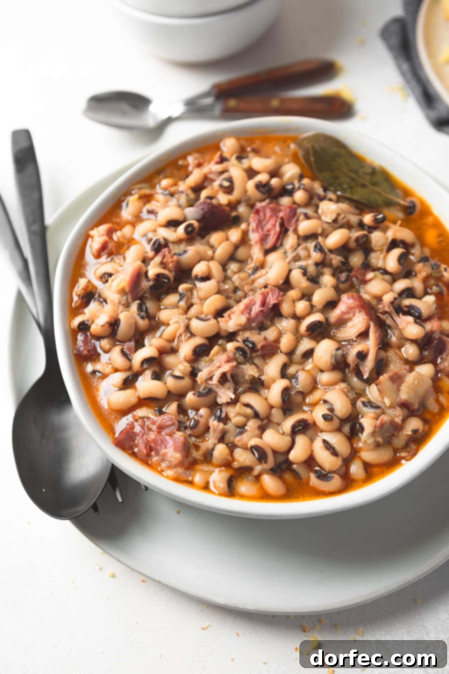 A close-up shot of a bowl of southern black eyed peas, steam gently rising, with a spoon and fork resting beside it. The inviting texture and rich color of the peas are highlighted, showcasing the dish's warmth and hearty appeal.