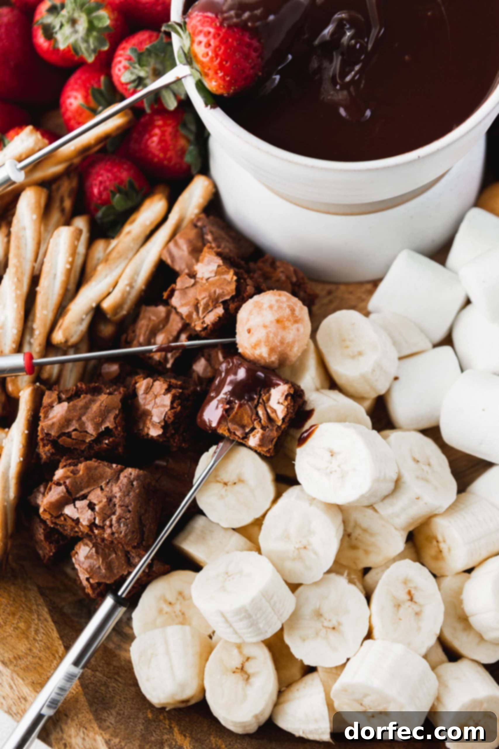 Fondue Dippers Assortment A picture of things to dip in chocolate fondue. There are bananas, strawberries, brownie bites, pretzels, and marshmallows around a bowl of chocolate fondue.