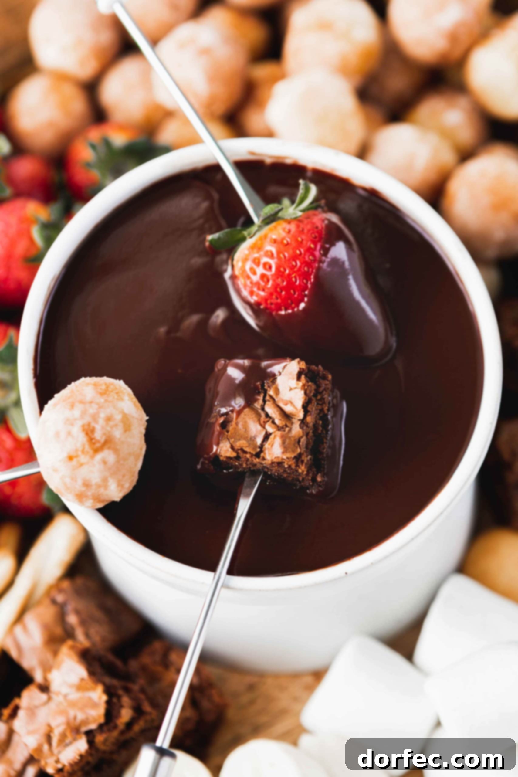 Chocolate Fondue Dipping A bowl of chocolate fondue with a strawberry, brownie bite, and a donut hole being dipped into the chocolate.
